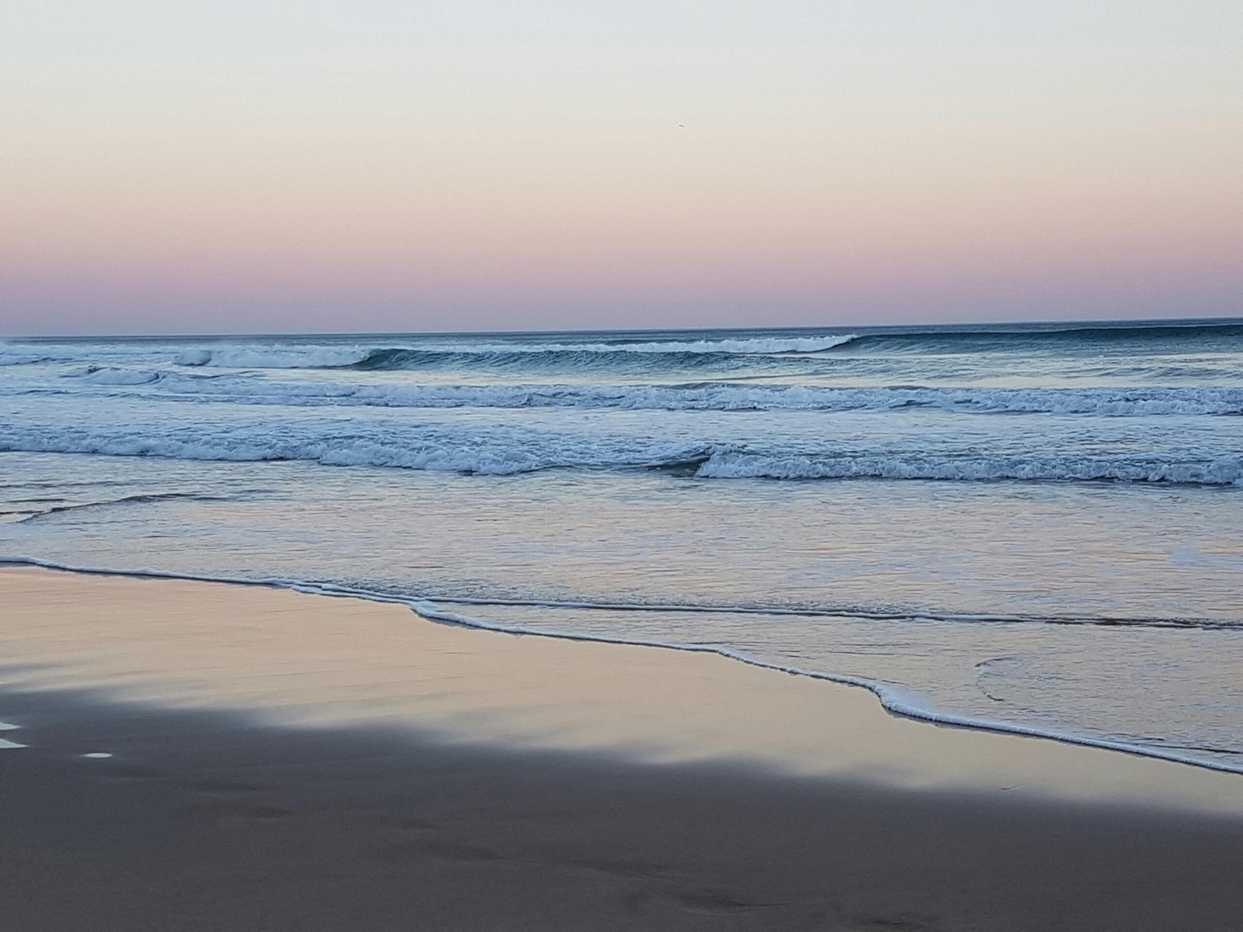image of waves crashing gently onto a beach at dusk