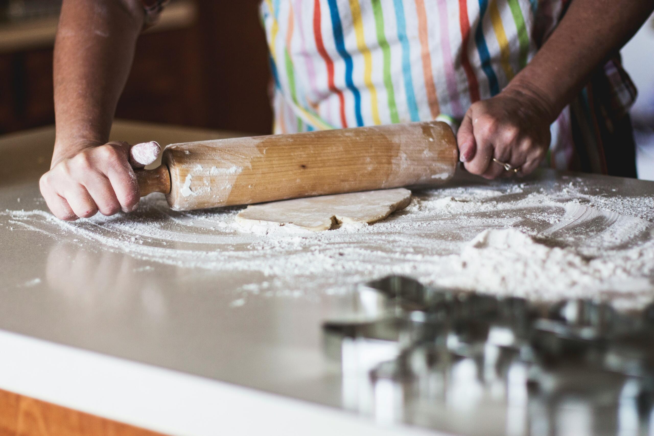 person holding a rolling pin rolling dough on floured surface