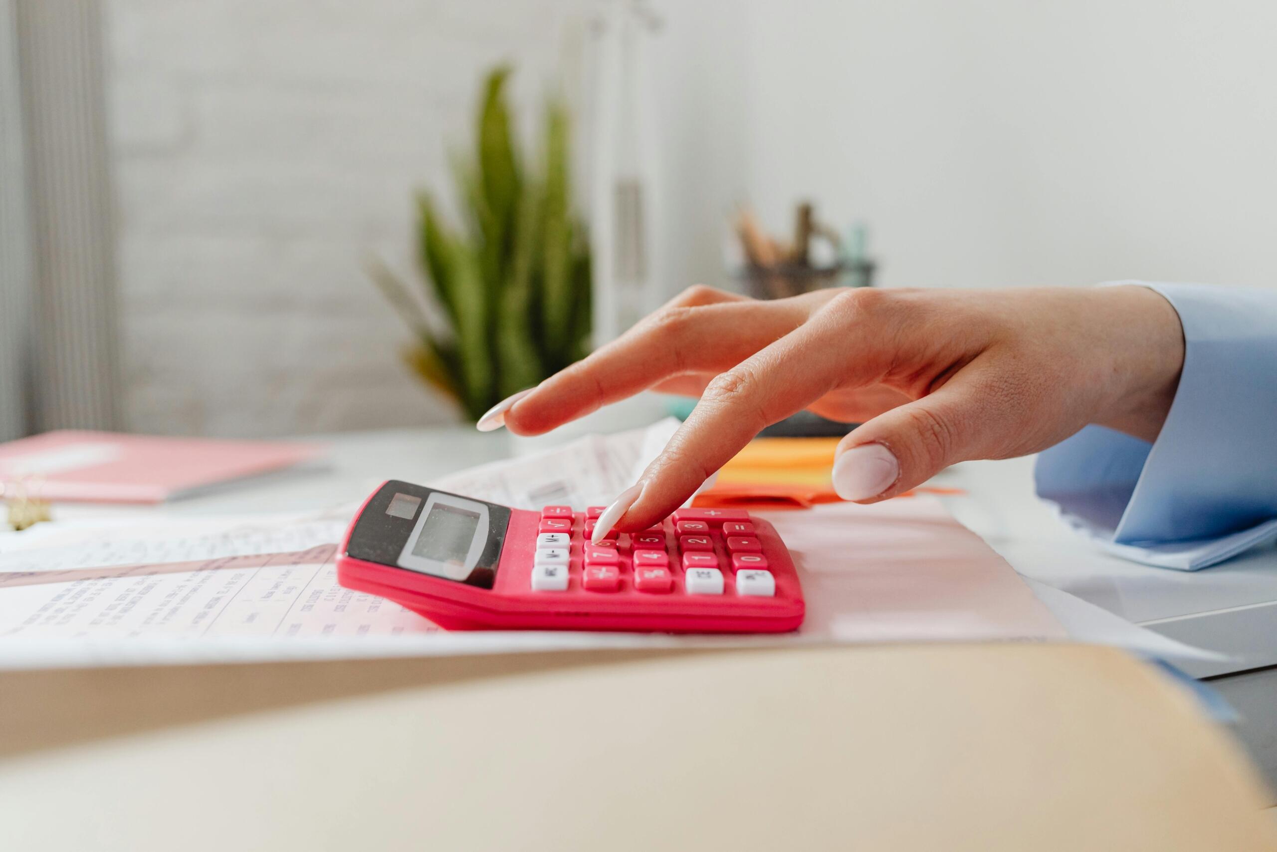 person with long painted fingernails using a red calculator