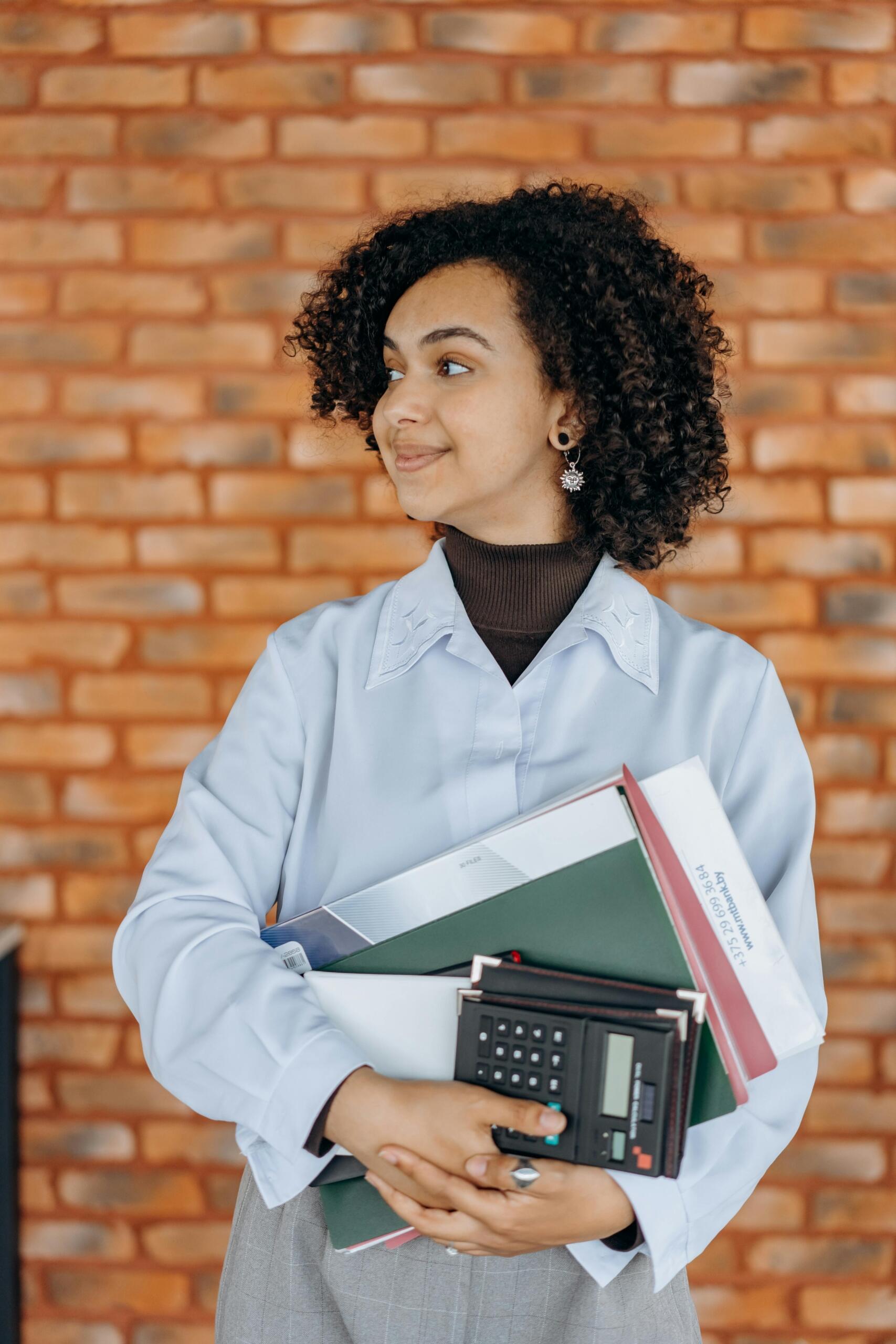 person in smart casual attire holding noteoks and a calculator