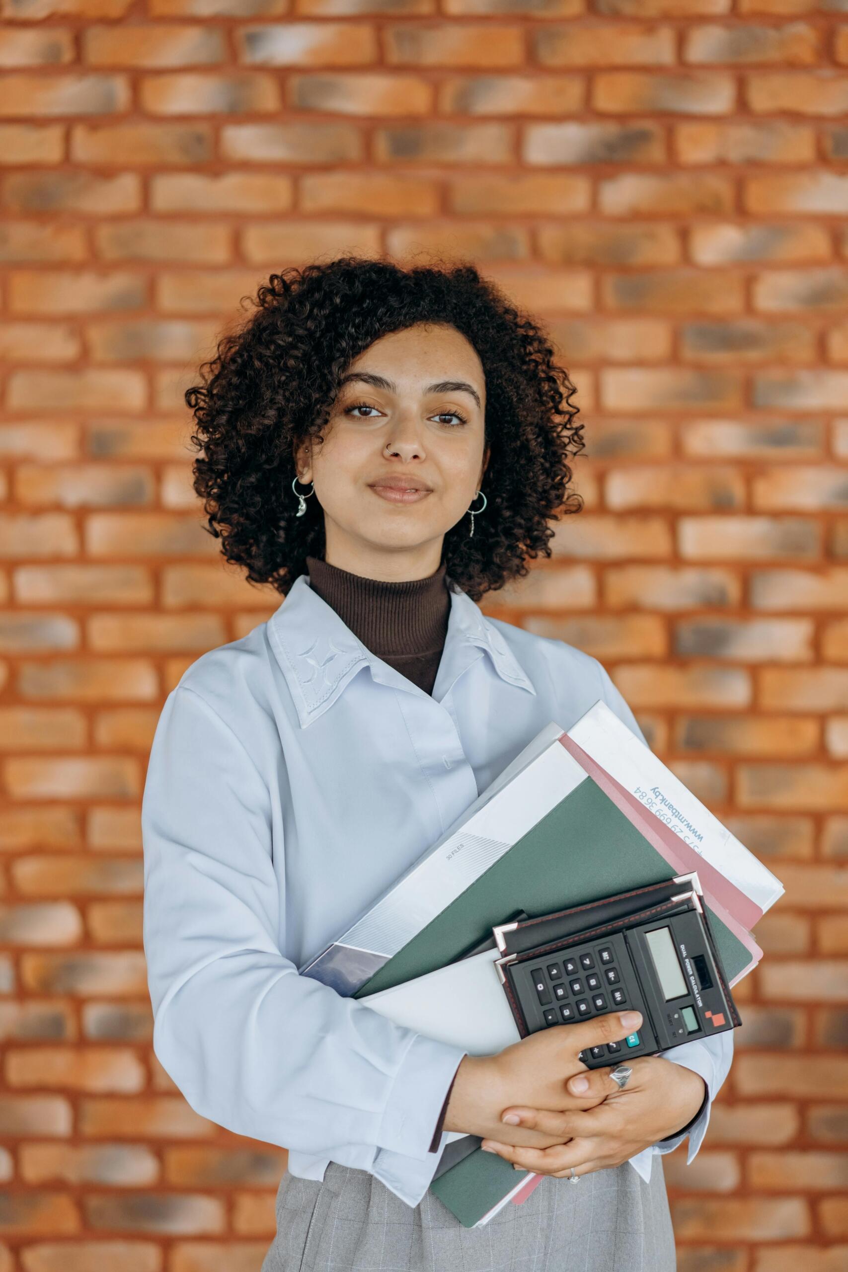 person in smart casual attire holding a calculator and notebooks
