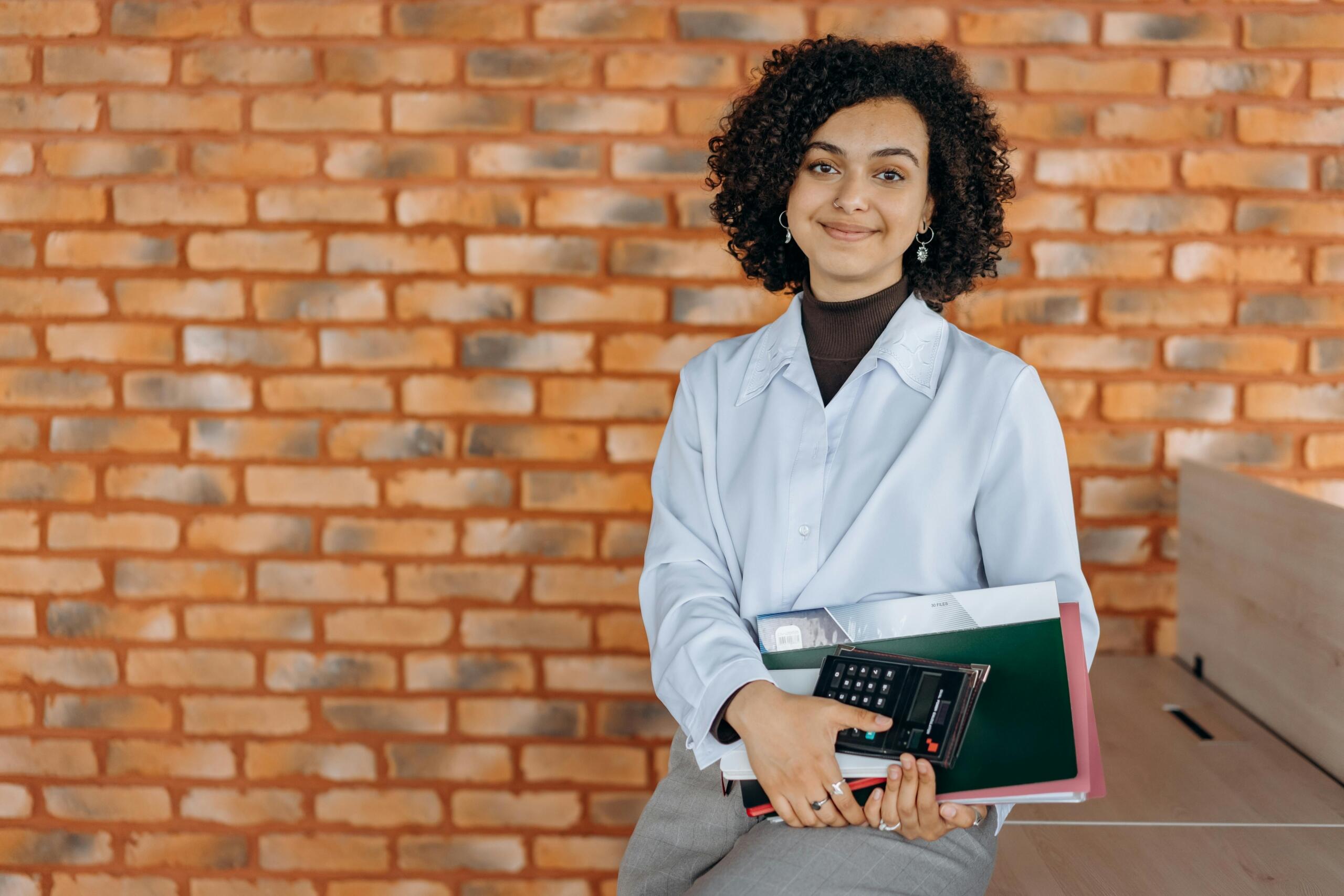 woman in smart casual attire holding notebooks and a calculator