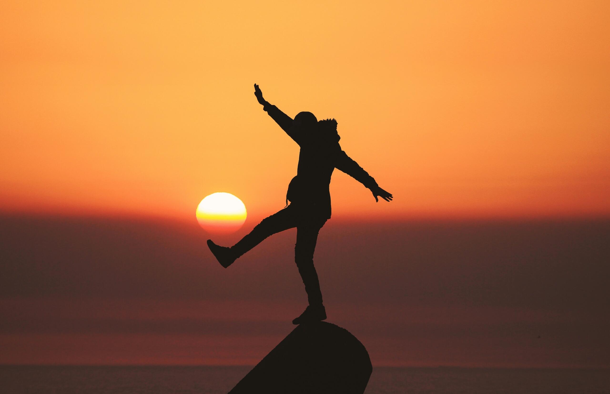 An image of a person balancing on a rock against a sunset.