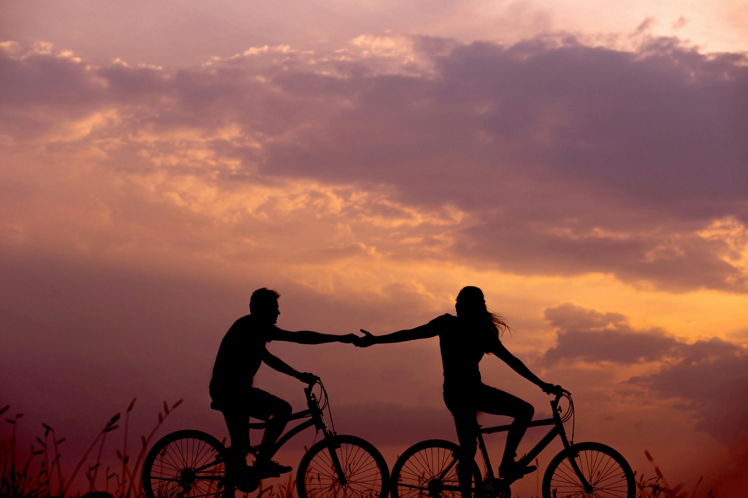 An image of a connected couple cycling against the sunset.