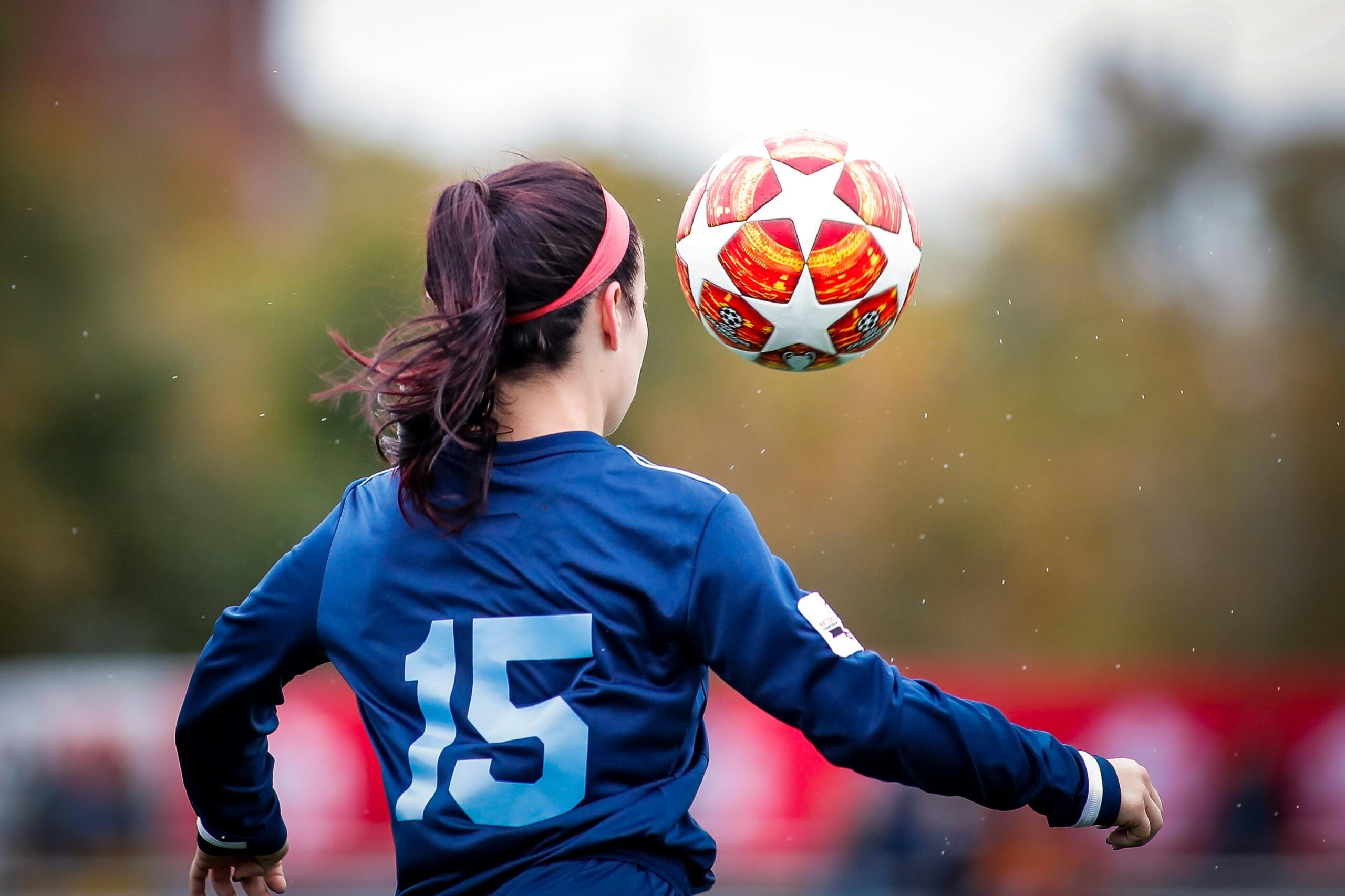 An image of a young woman kicking a soccer ball in the air.