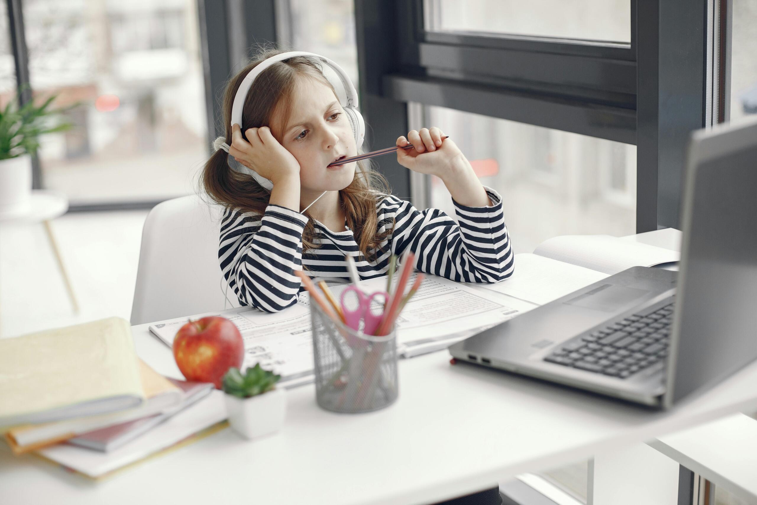 girl sitting at a desk using a laptop and wearing headphpones