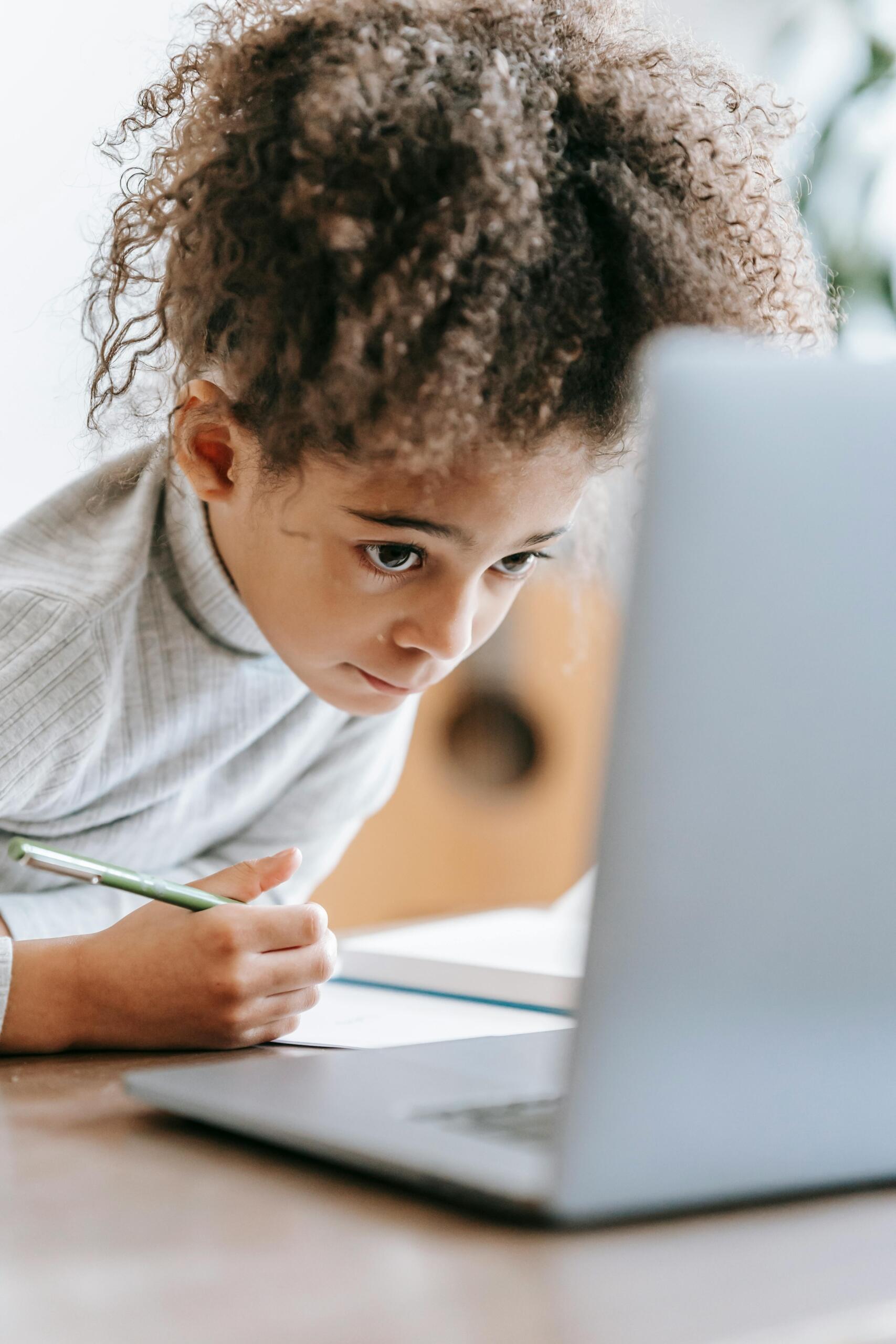 girl sitting at a desk, making notes and using a laptop
