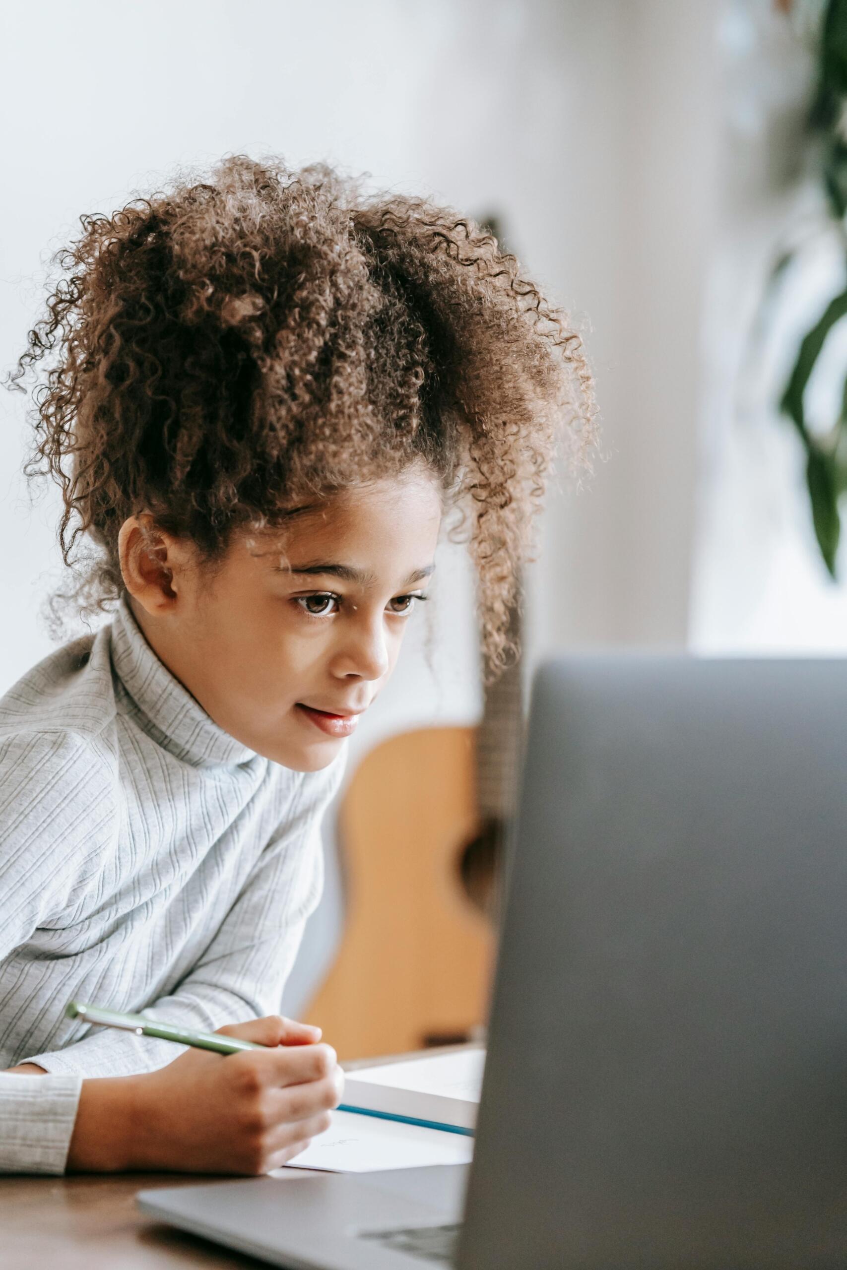 girl sitting at a desk, making notes and using a laptop