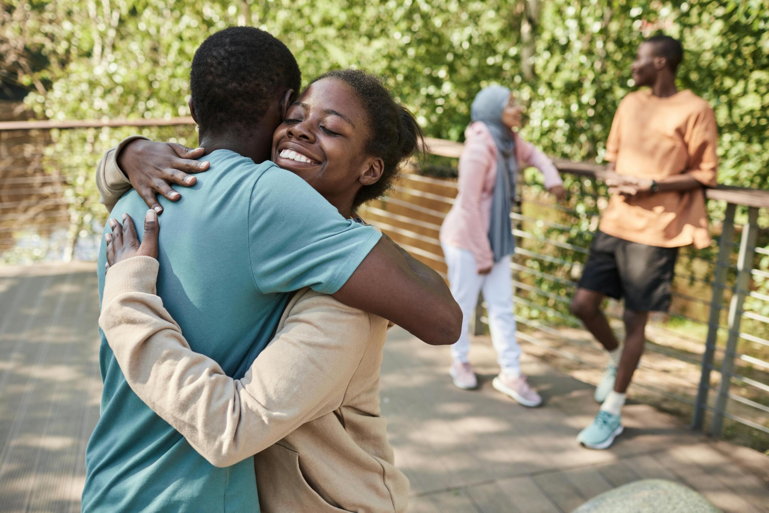 two teenage friends giving each other a hug while their other friends chatin the background