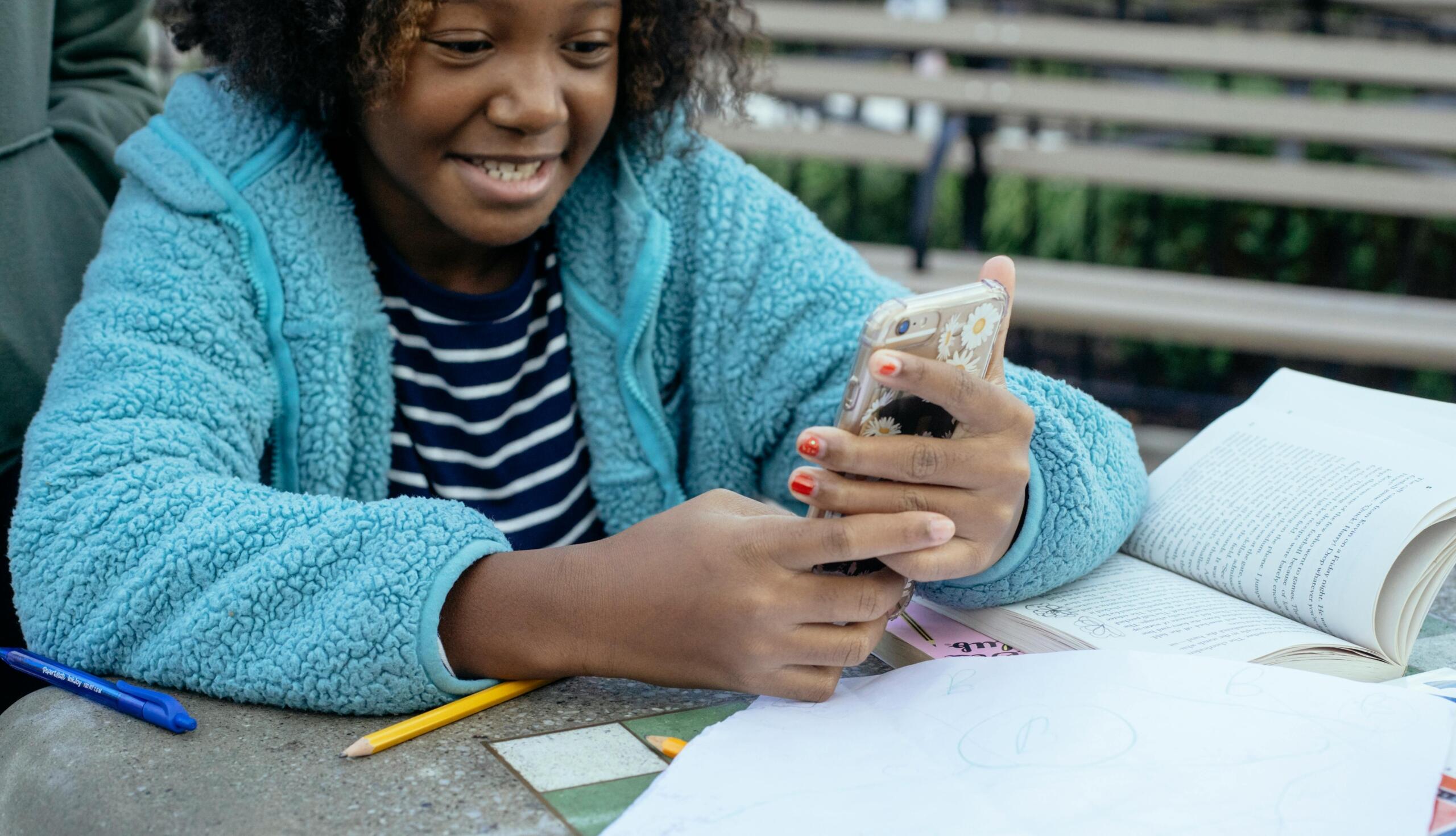 girl sitting at a table using a smartphone to do homework