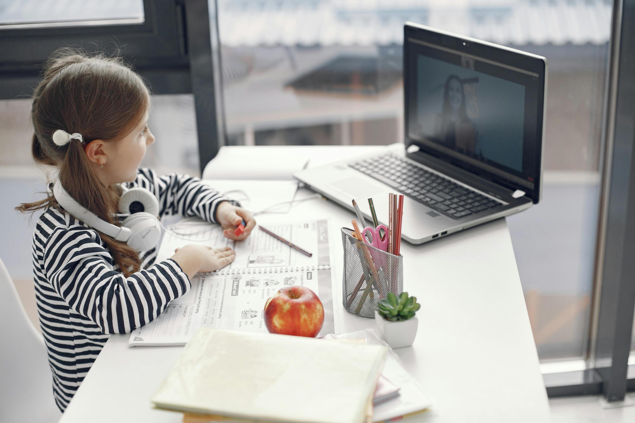 girl sitting at a desk using a laptop for an online lesson with a teacher