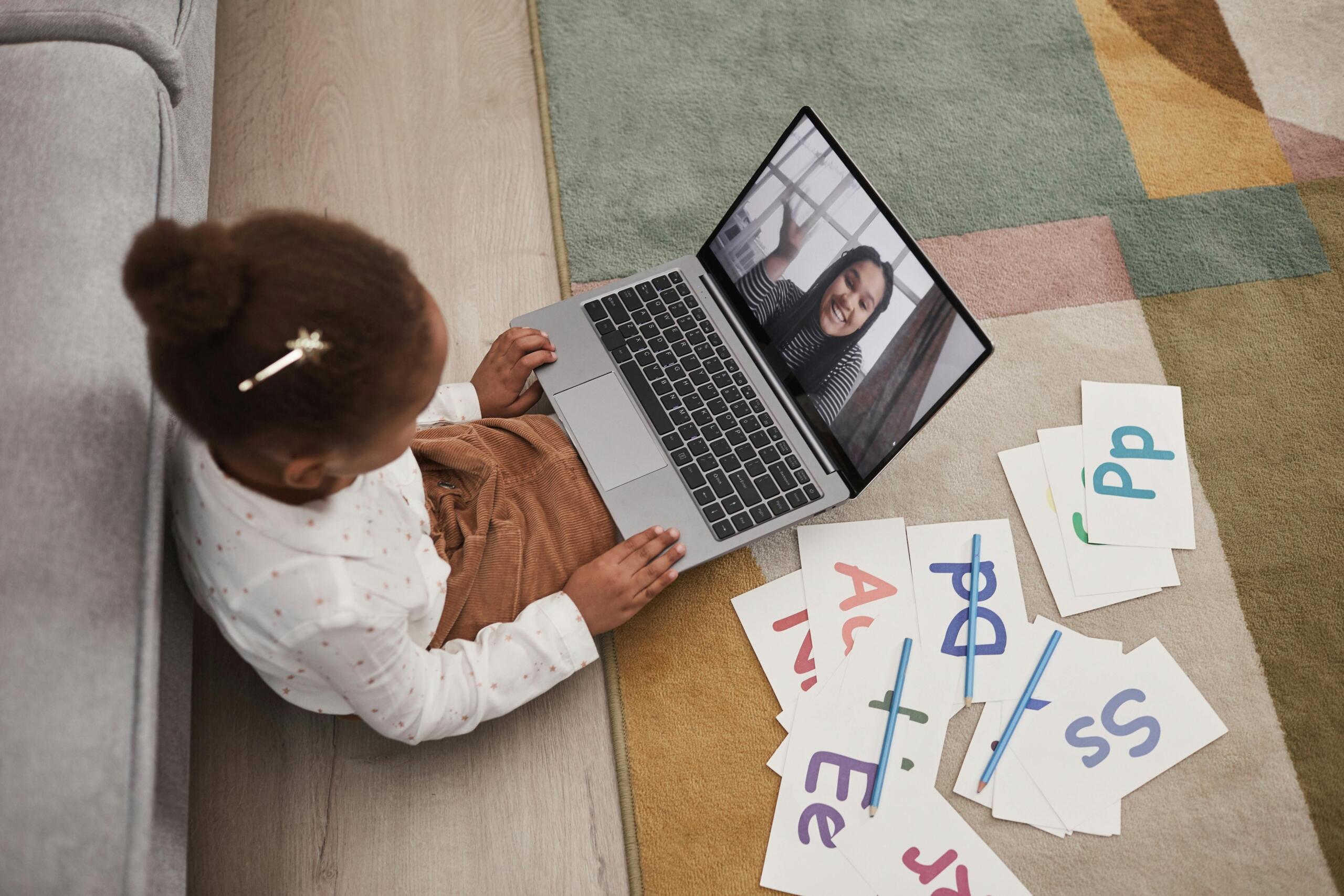 young girl using a laptop for an online lesson with a teacher, with alphabet flashcards next to her