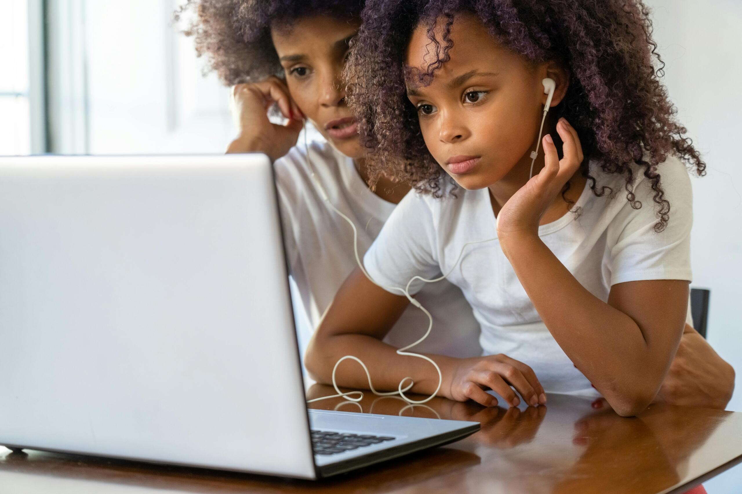 child sitting with mom sharing earphones and using a laptop