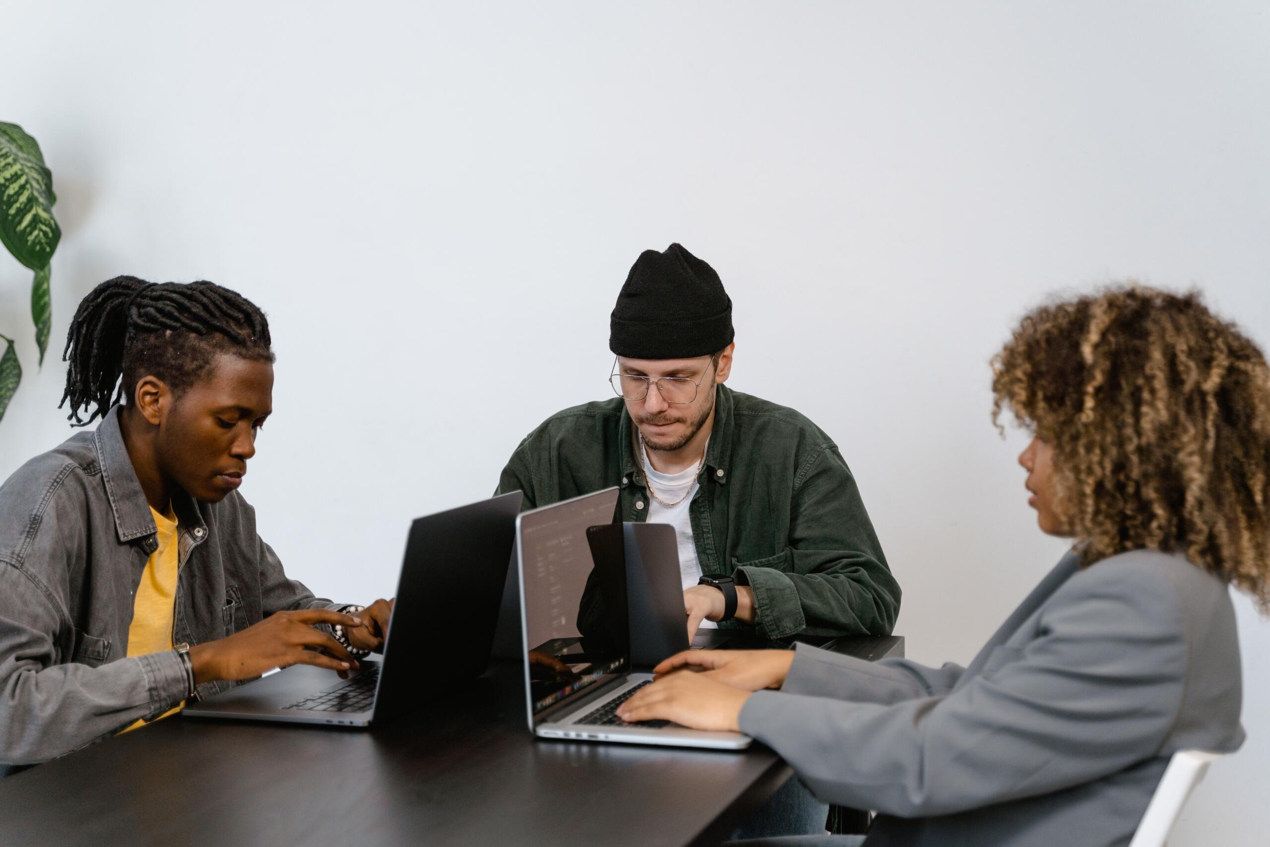three people sitting at a table all working on laptops