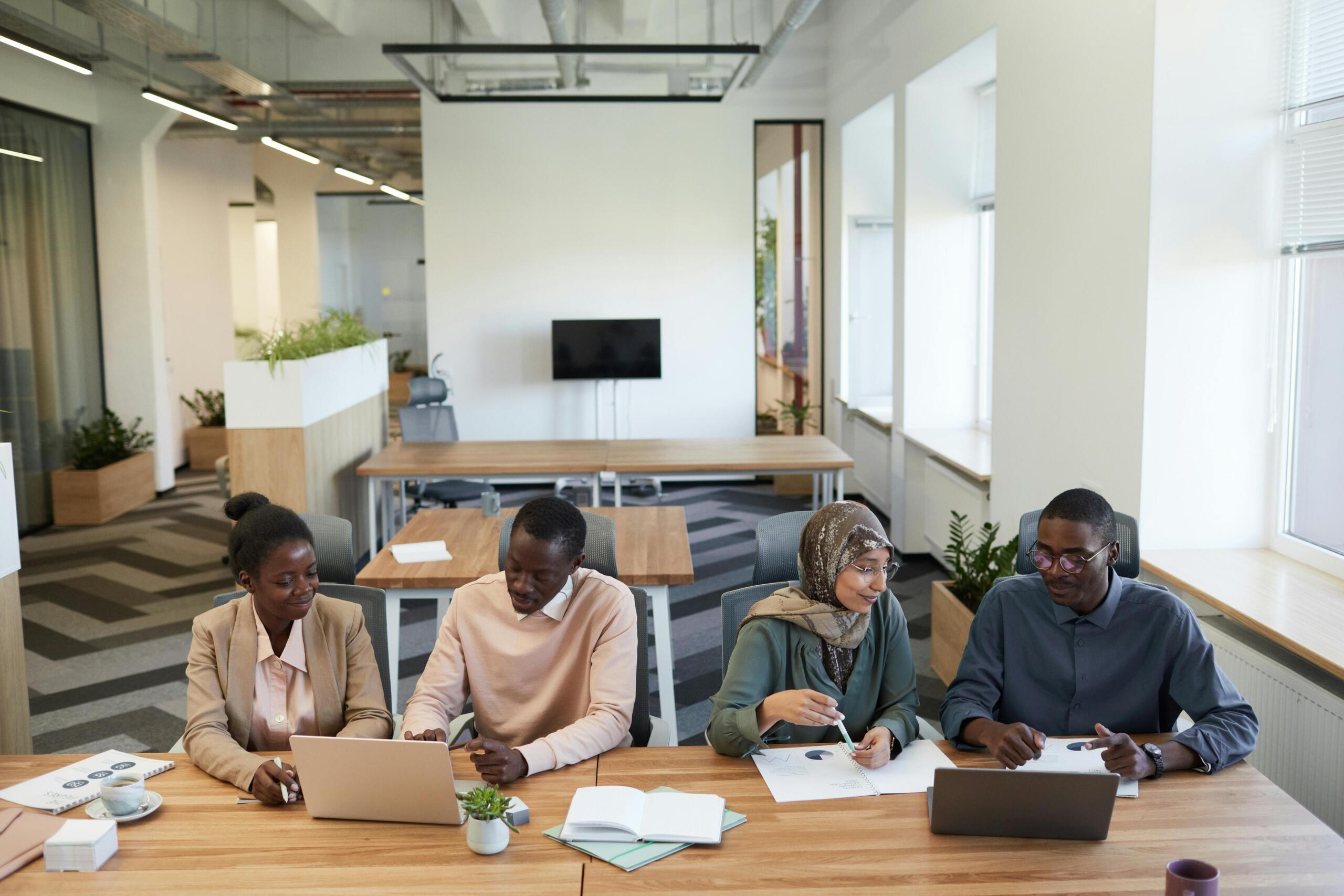 four people sitting at a table working on laptops