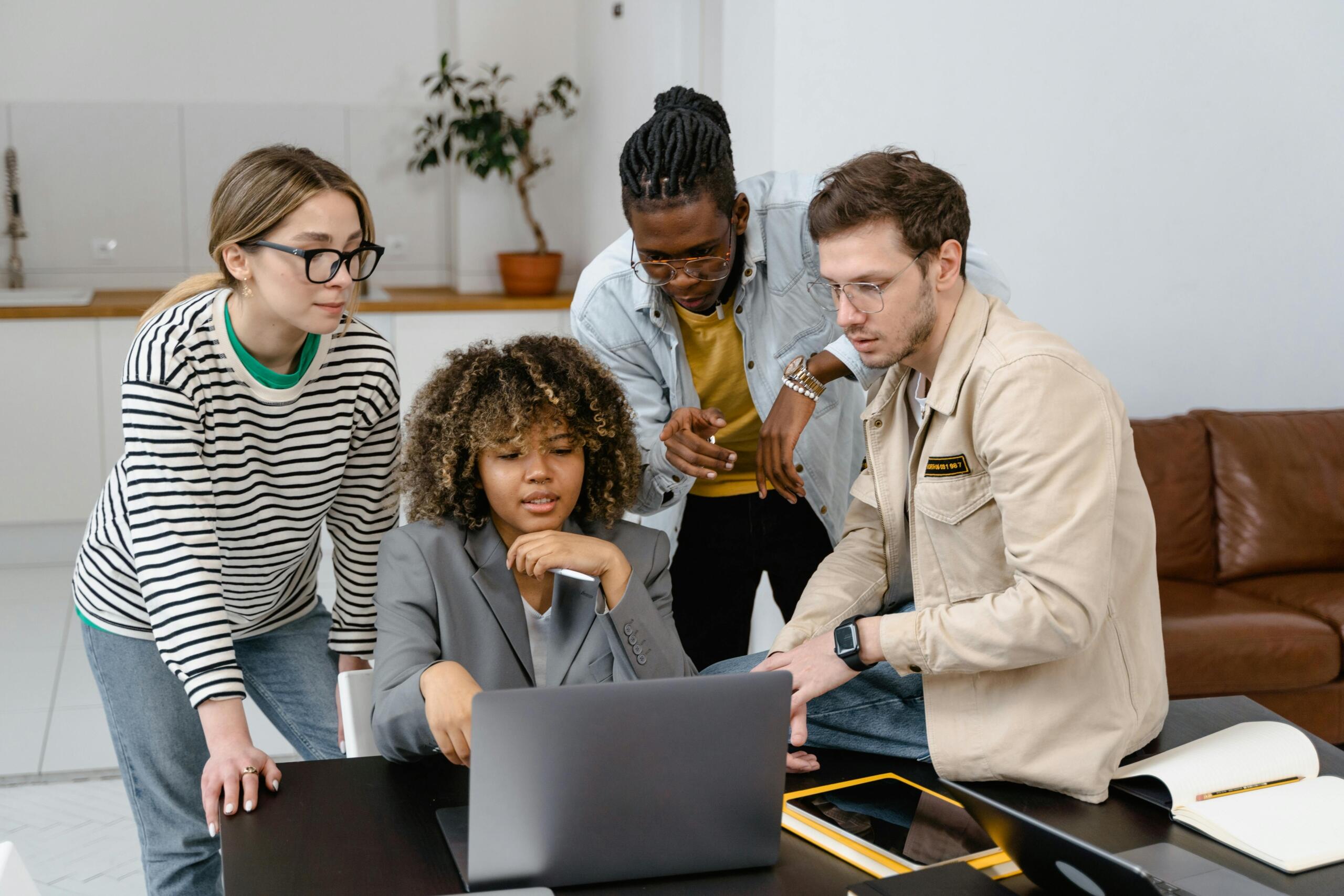 four people gathered around a table looking at one laptop screen