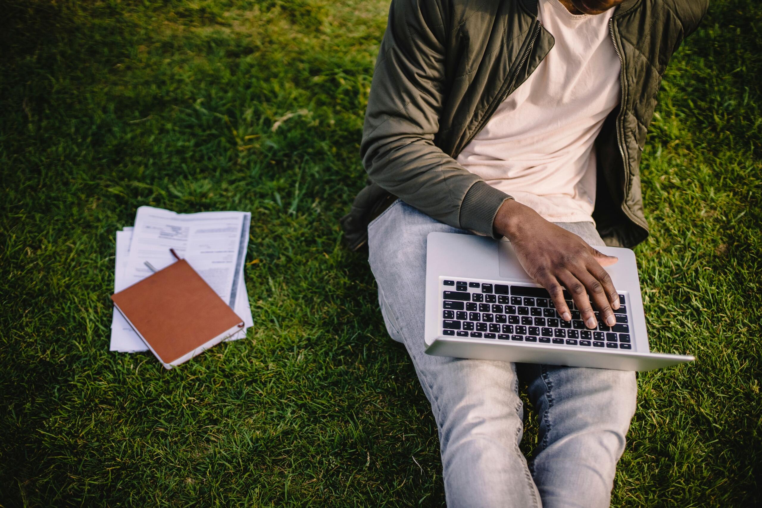 A cropped image of a student studying on the grass with a laptop.