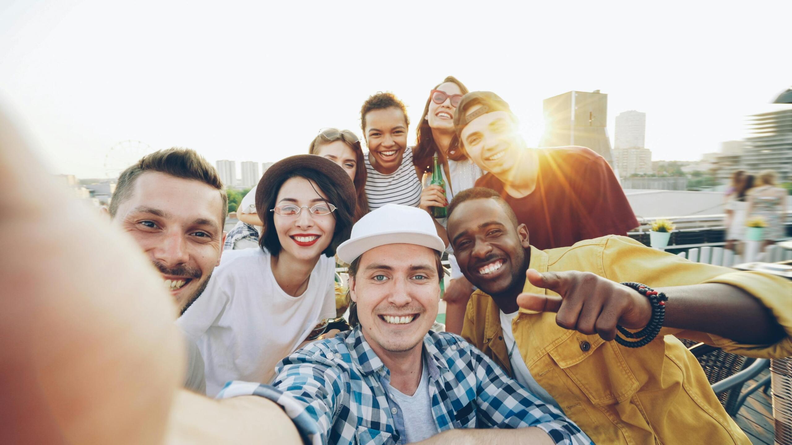 A diverse group of smiling friends taking a selfie on a rooftop at sunset