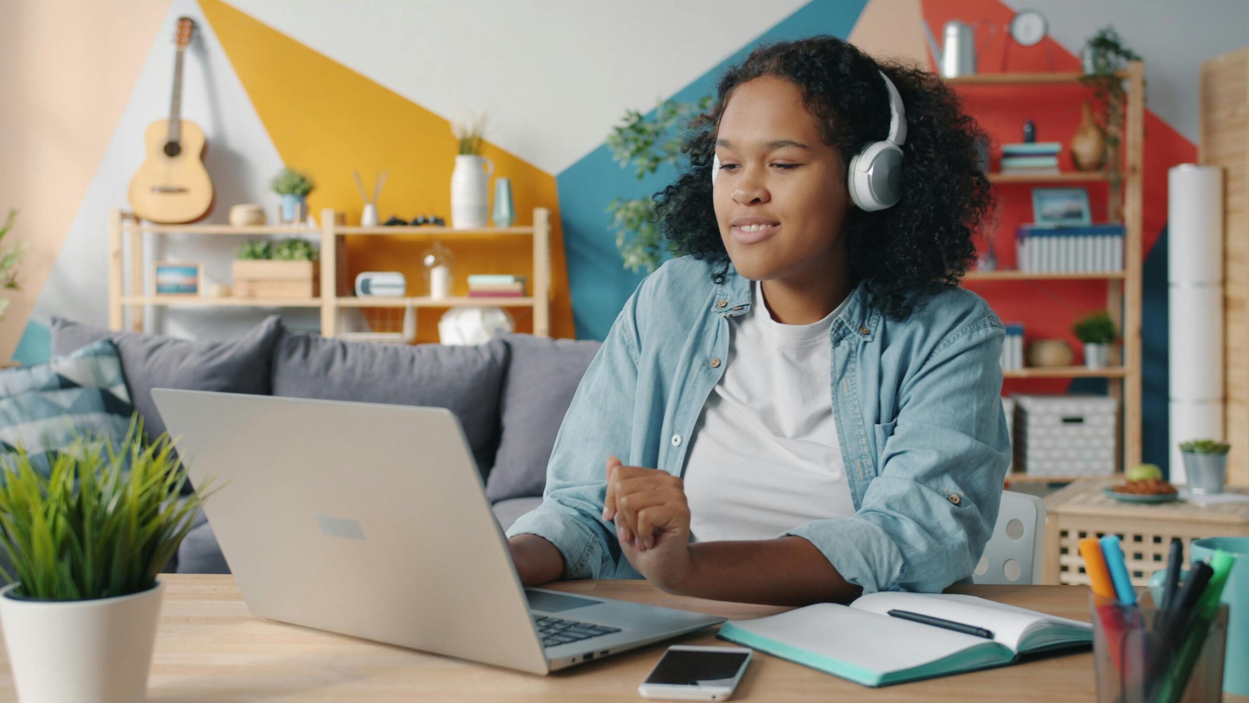 teen sitting at a desk using a laptop and wearing headphones