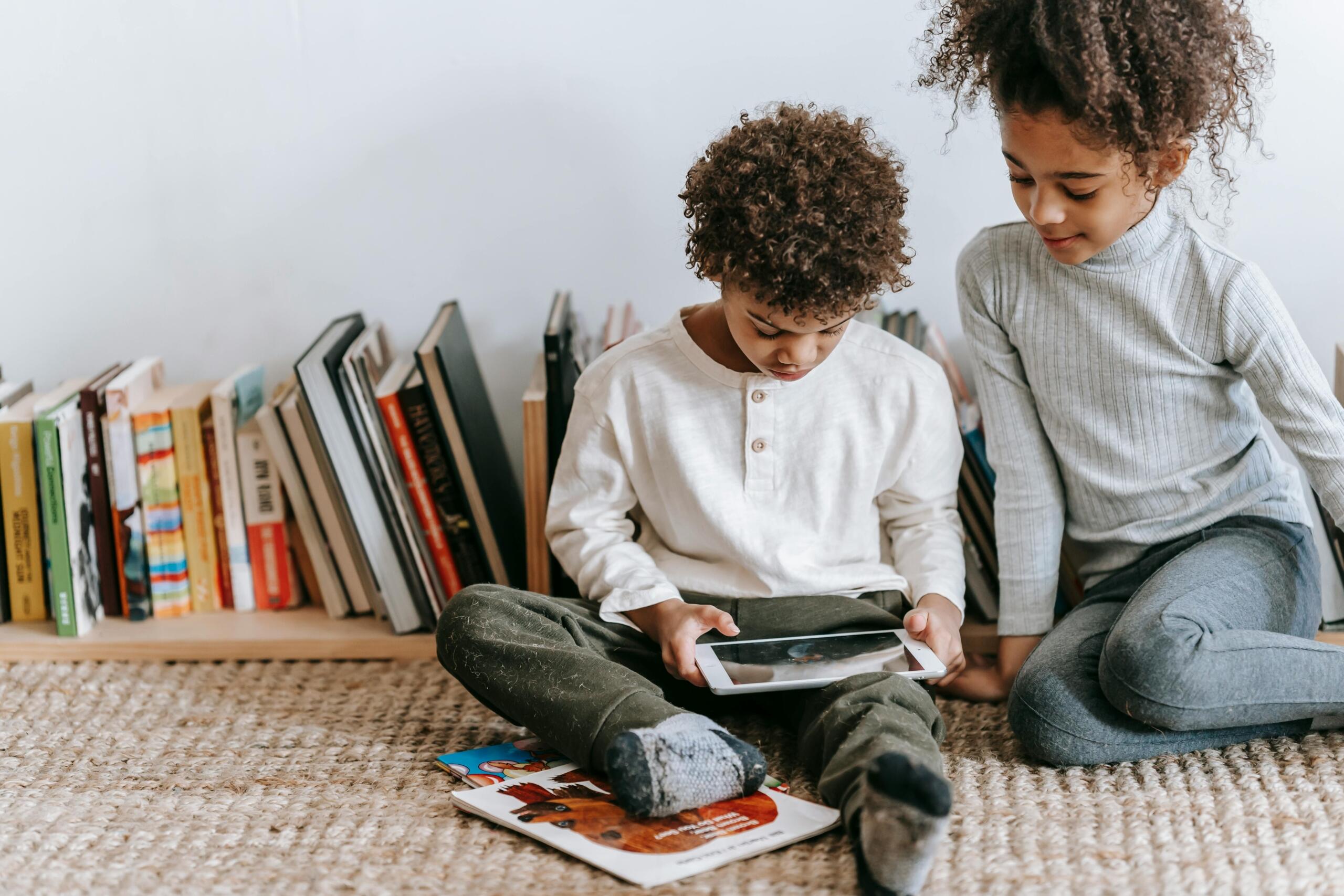 boy and girl sitting on the floor looking at an ipad