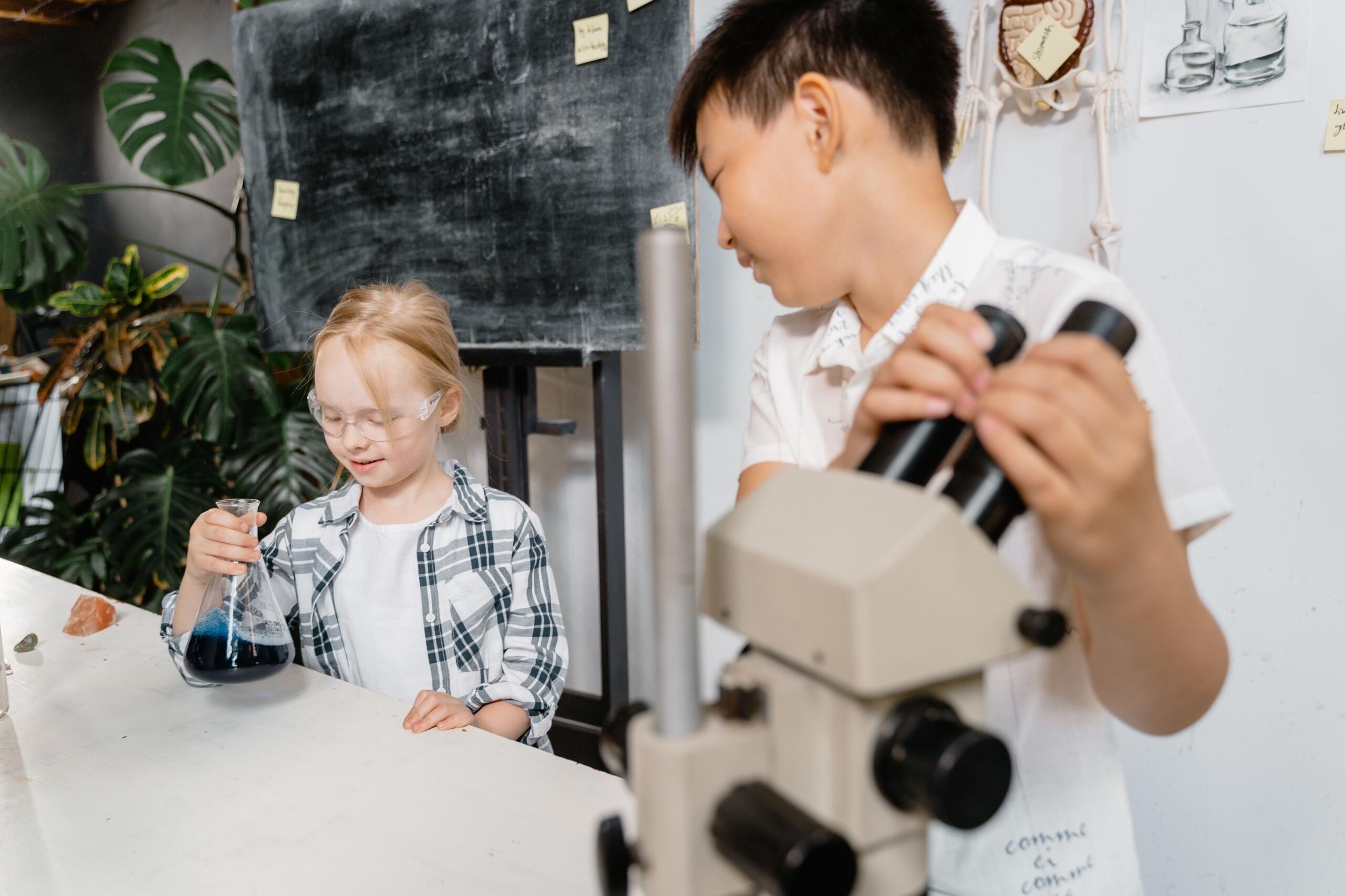 girl mixing liquids in beaker while boy uses microscope