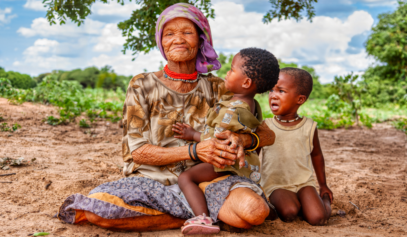 San woman sitting under a tree with two children