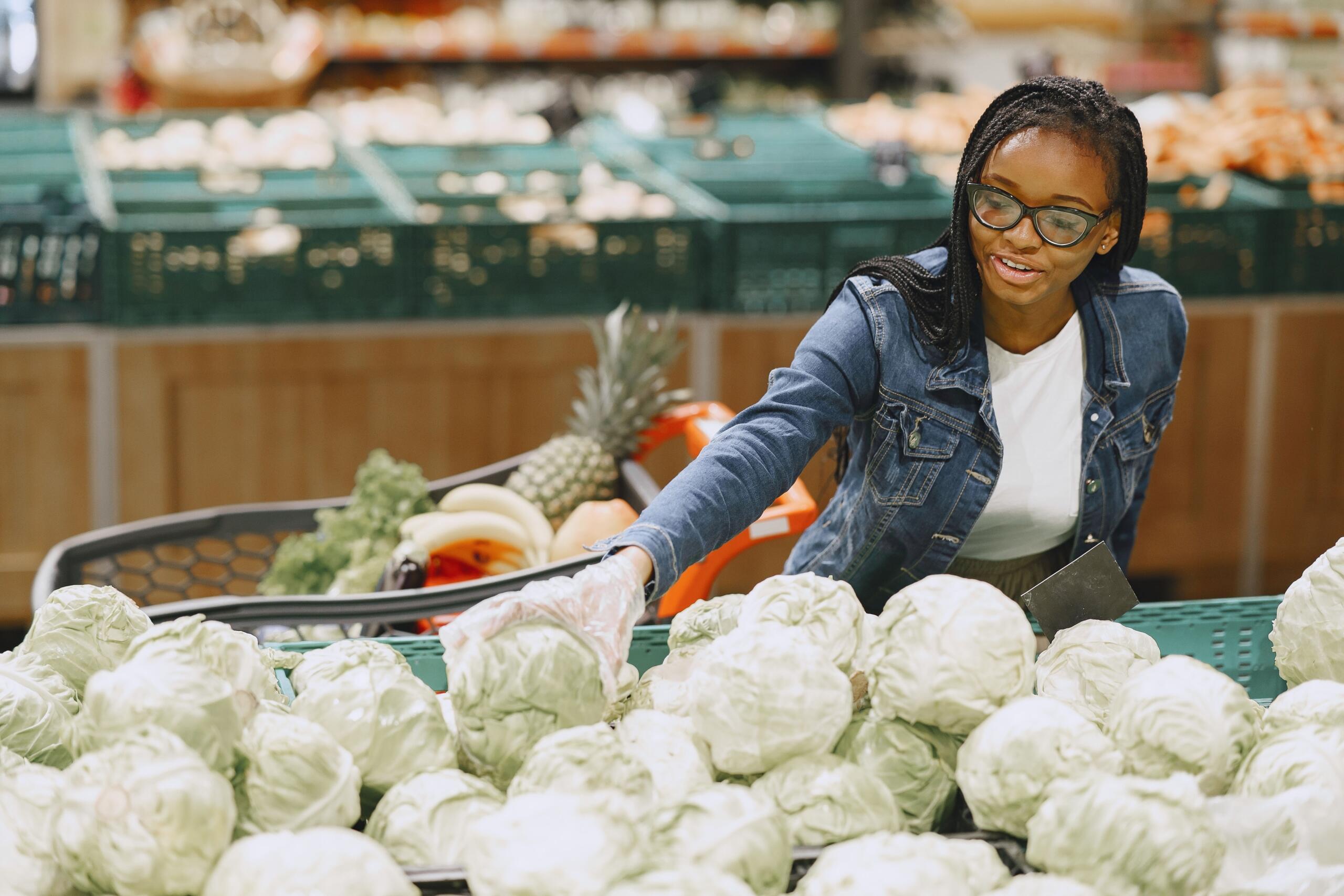 An image of a woman choosing a cabbage in a grocery store.