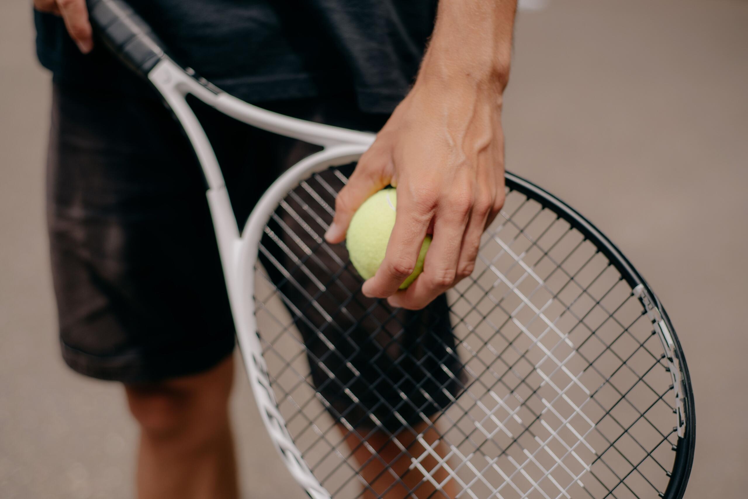 A close up image of a tennis player holding a ball and racket, ready to serve.