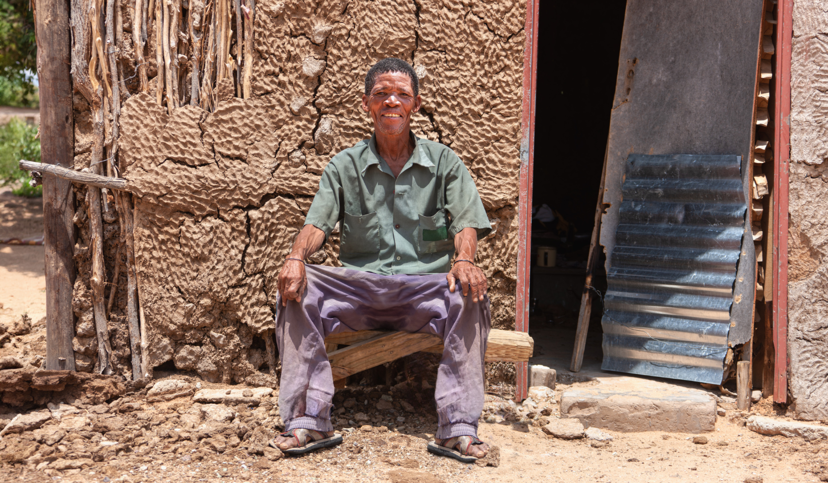 smiling Khoisan man sitting in front of his traditional home