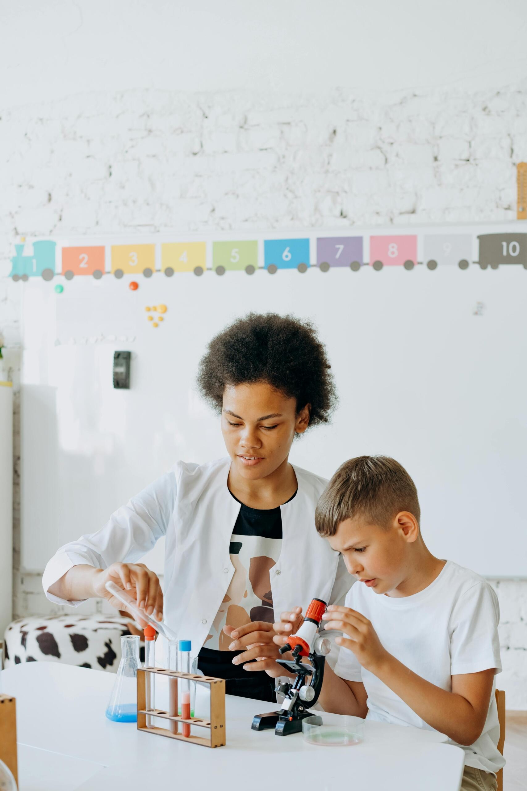 teacher mixing liquids in test tubes while student uses microscope