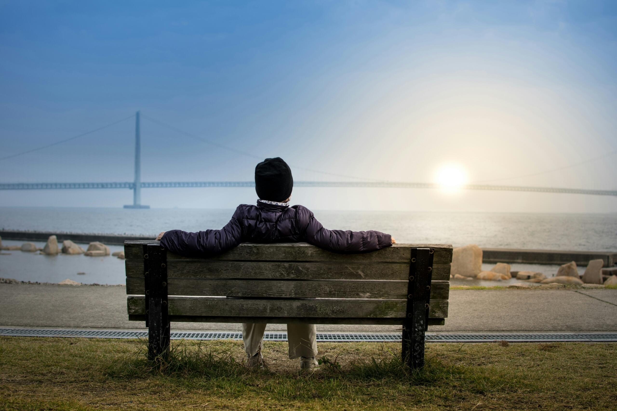 An image of a person sitting on a bench watching the sun set over the ocean.
