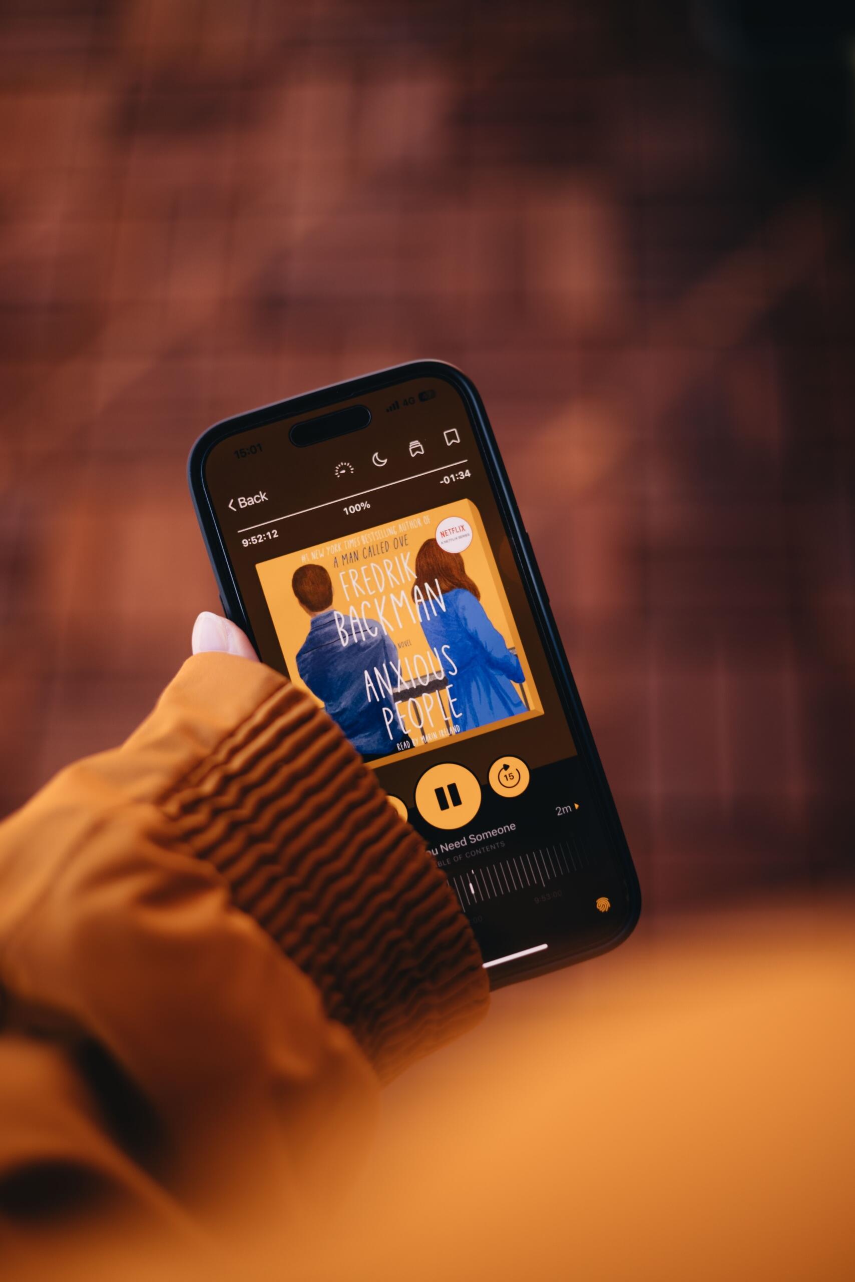 person holding a smartphone with the cover of an audiobook displayed on the screen