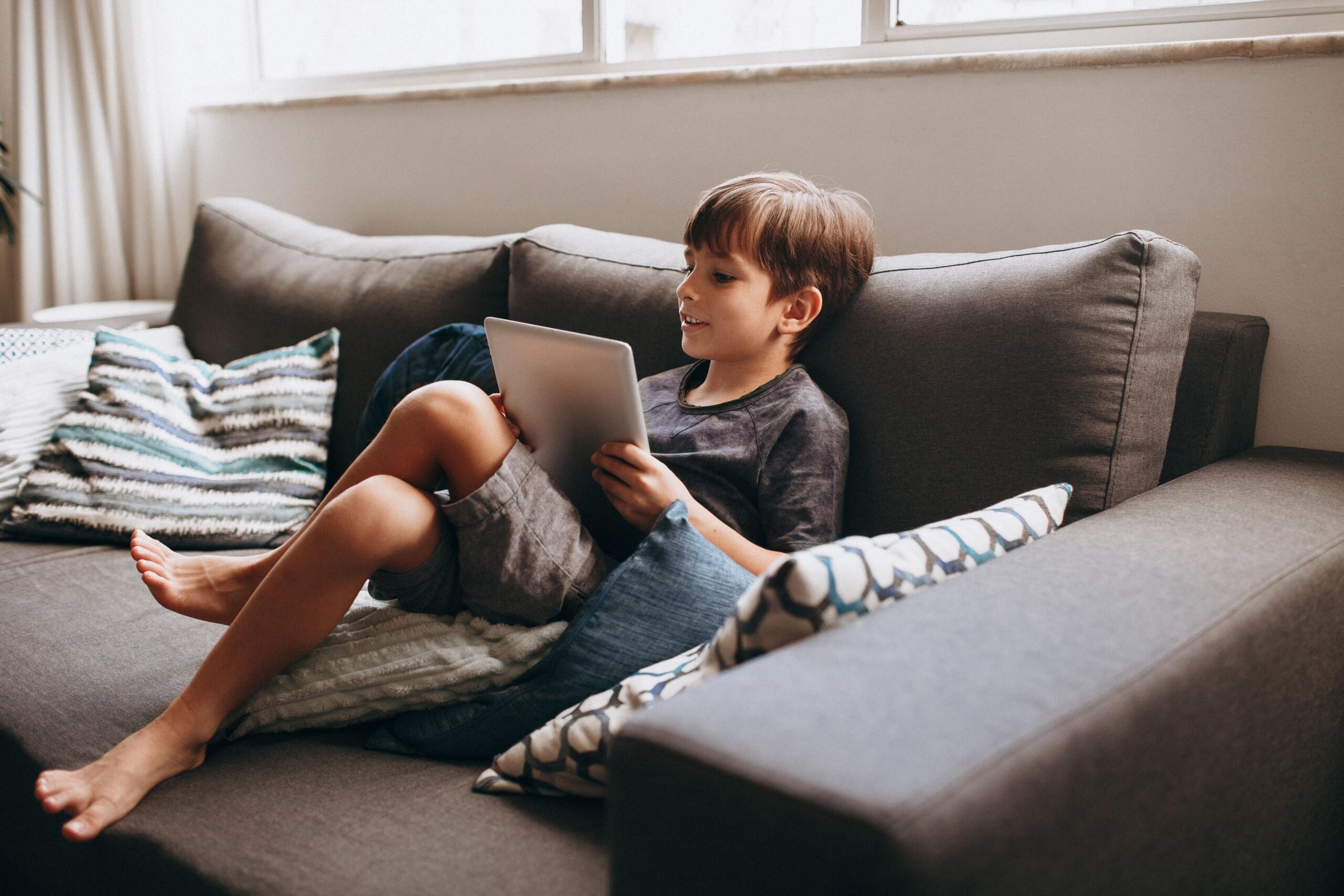 child sitting on a couch reading on e-reader