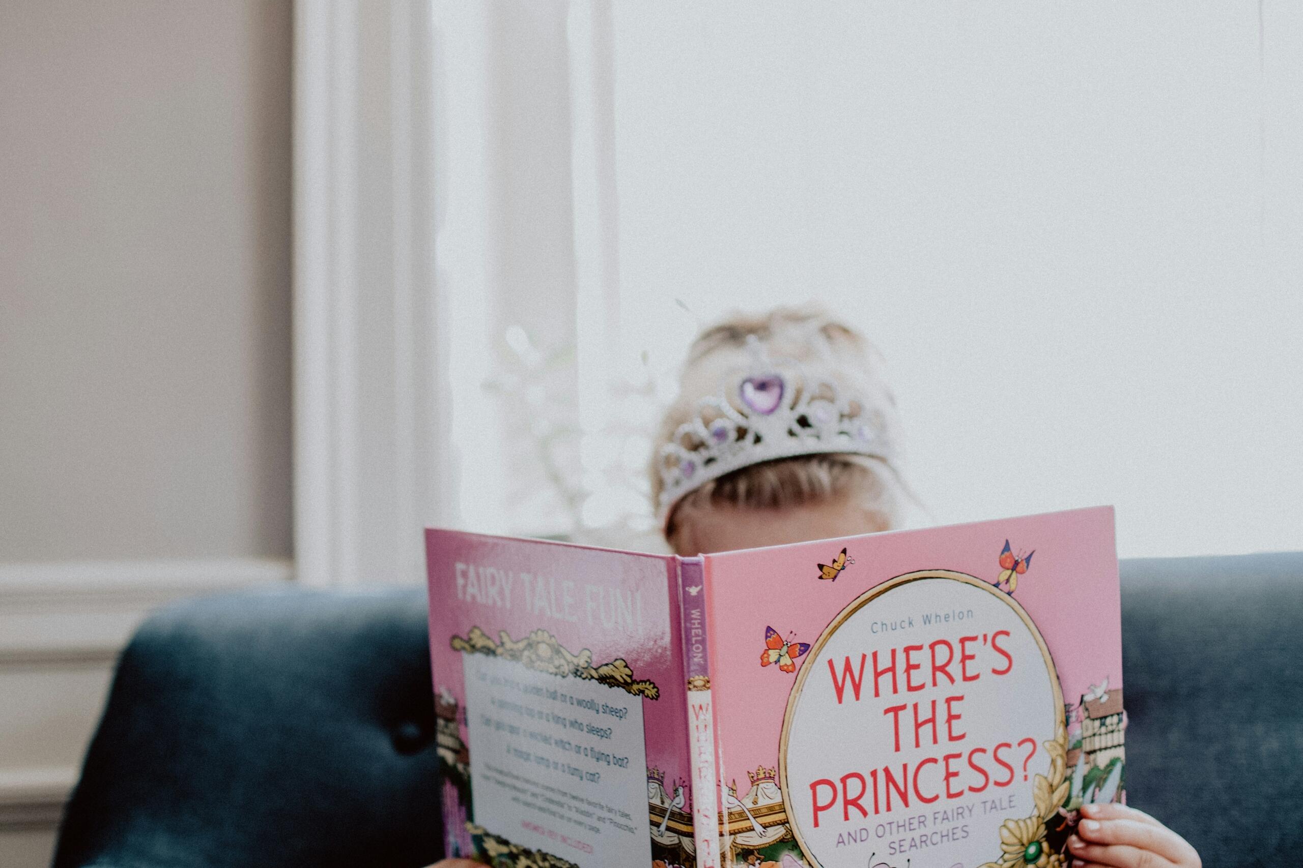 young girl wearing a tiara and reading a princess book