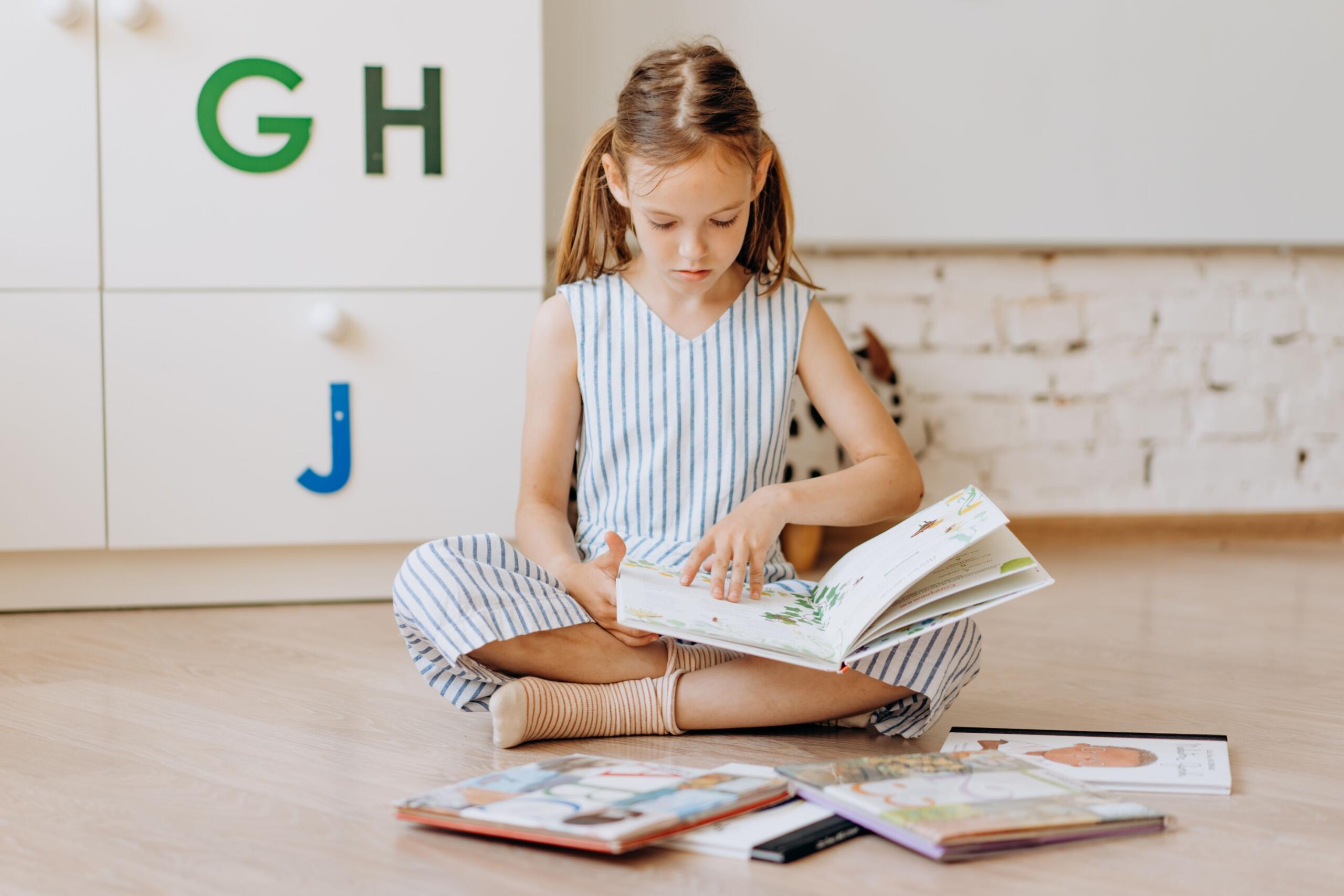 young girl sitting on the floor reading with a selection of books placed in front of her
