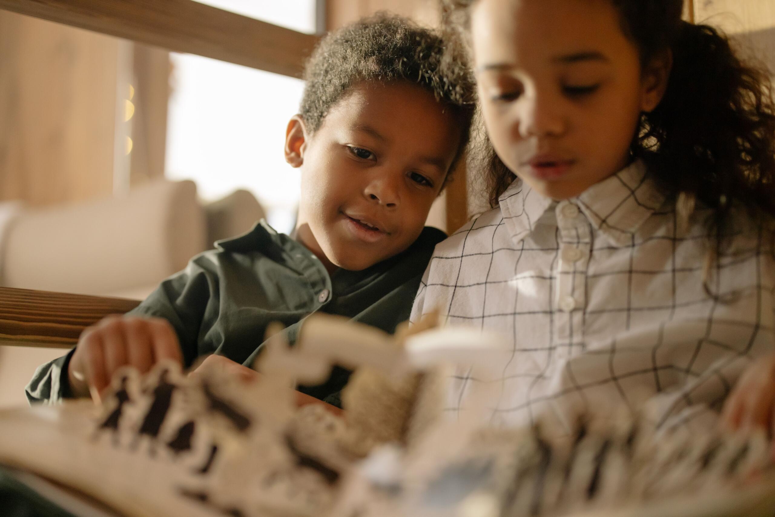 a boy and a girl seated on a couch reading a pop-up book