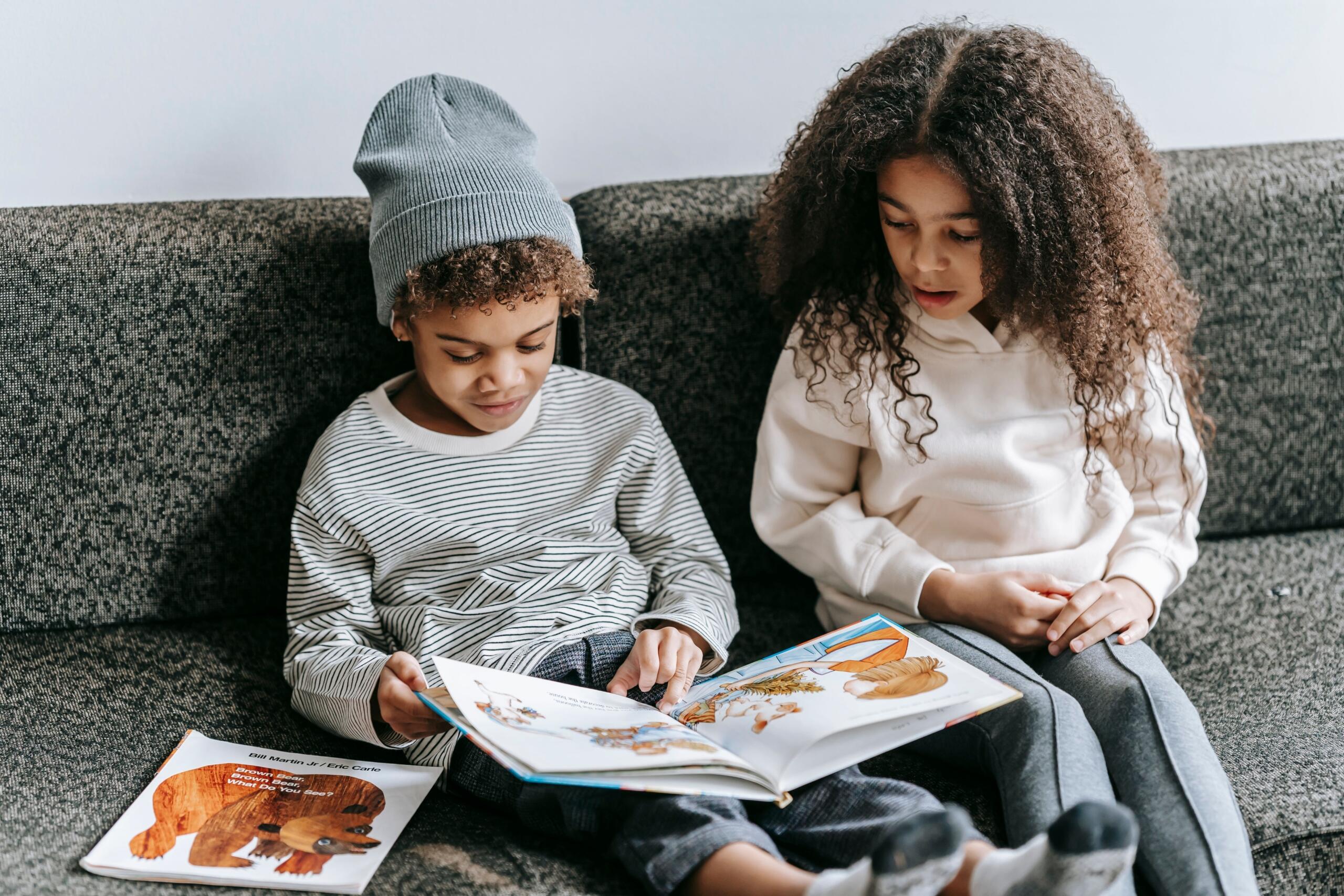 a boy and a girl seated on a couch reading the same children's book
