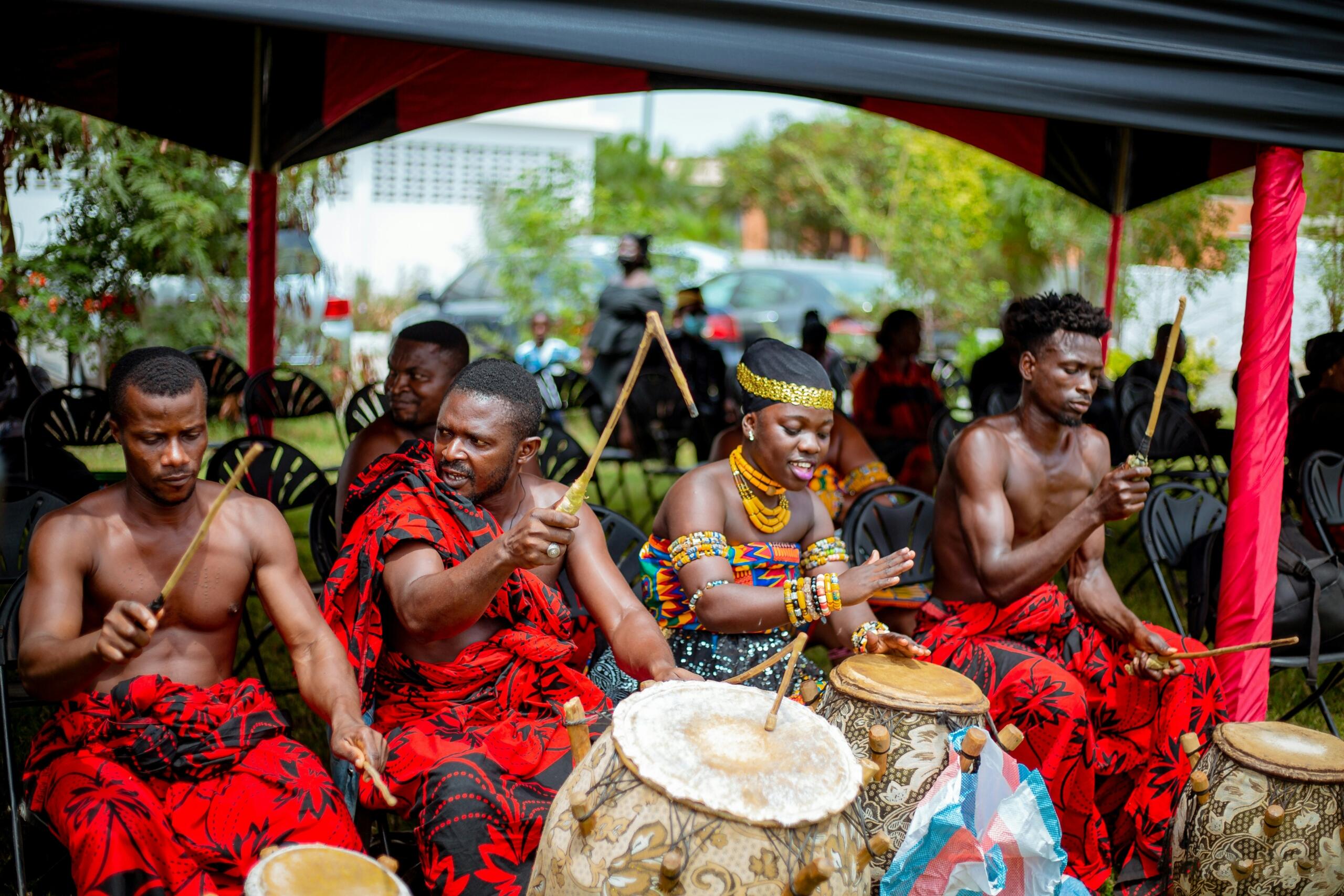 Traditional African musicians performing together on drums at an outdoor cultural event.
