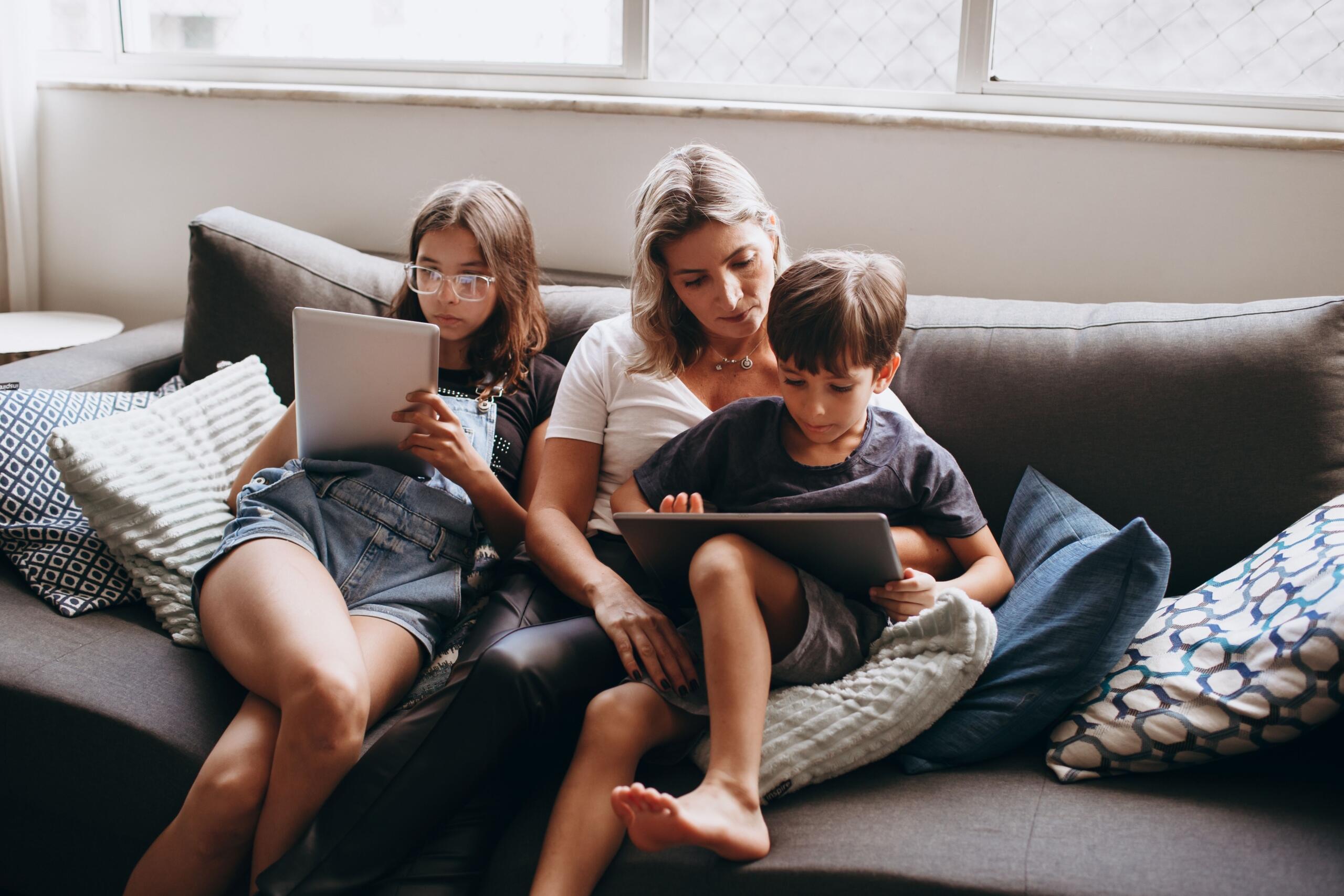 mom, son and daughter sitting on a couch reading on e-readers