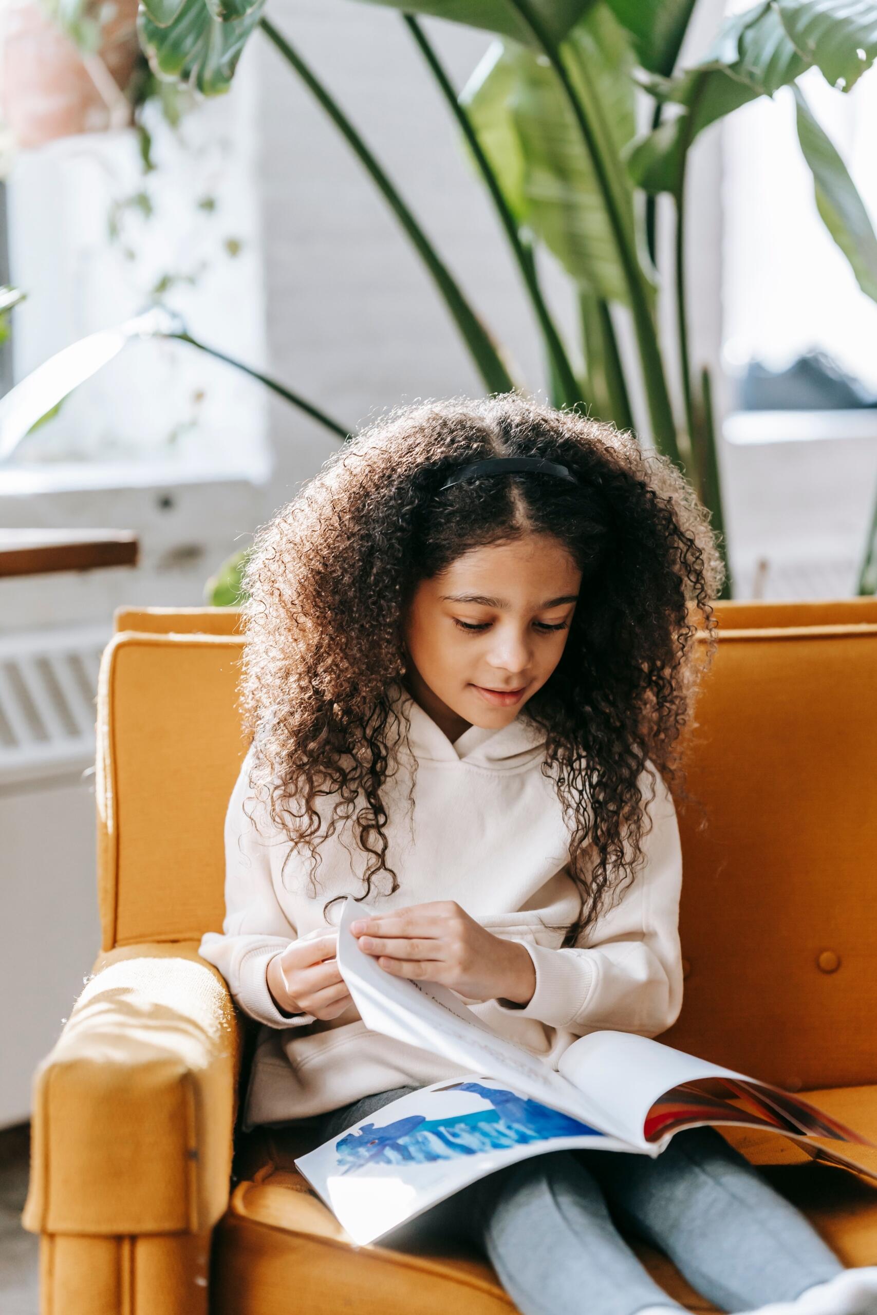 young girl sitting on an orange sofa reading a book with pictures