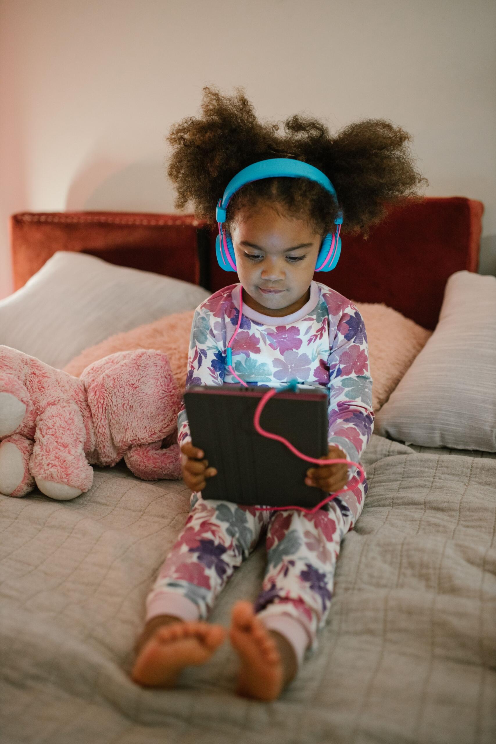 young child wearing headphones plugged into a tablet
