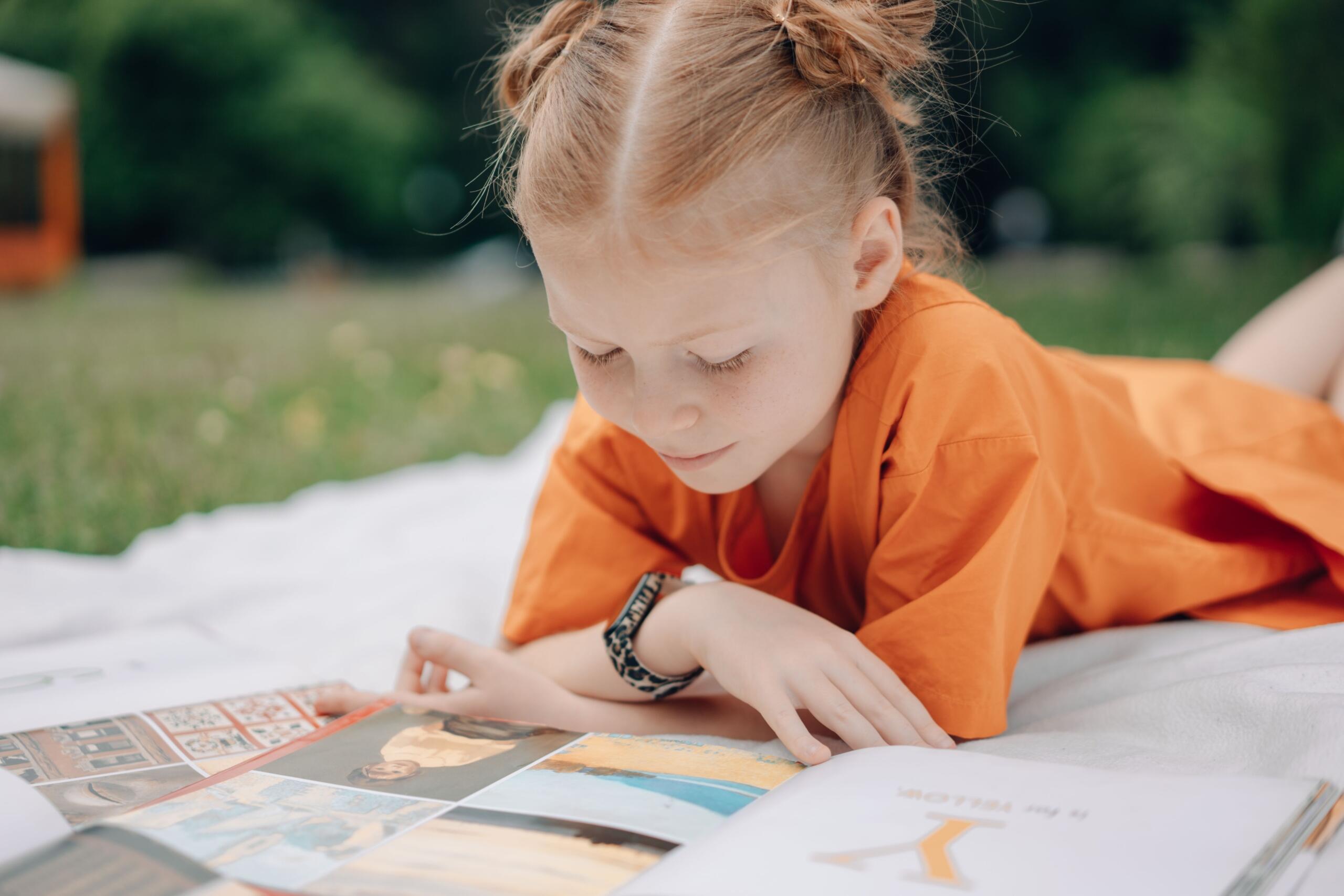 young girl lying on a picnic blanket reading an illustrated book