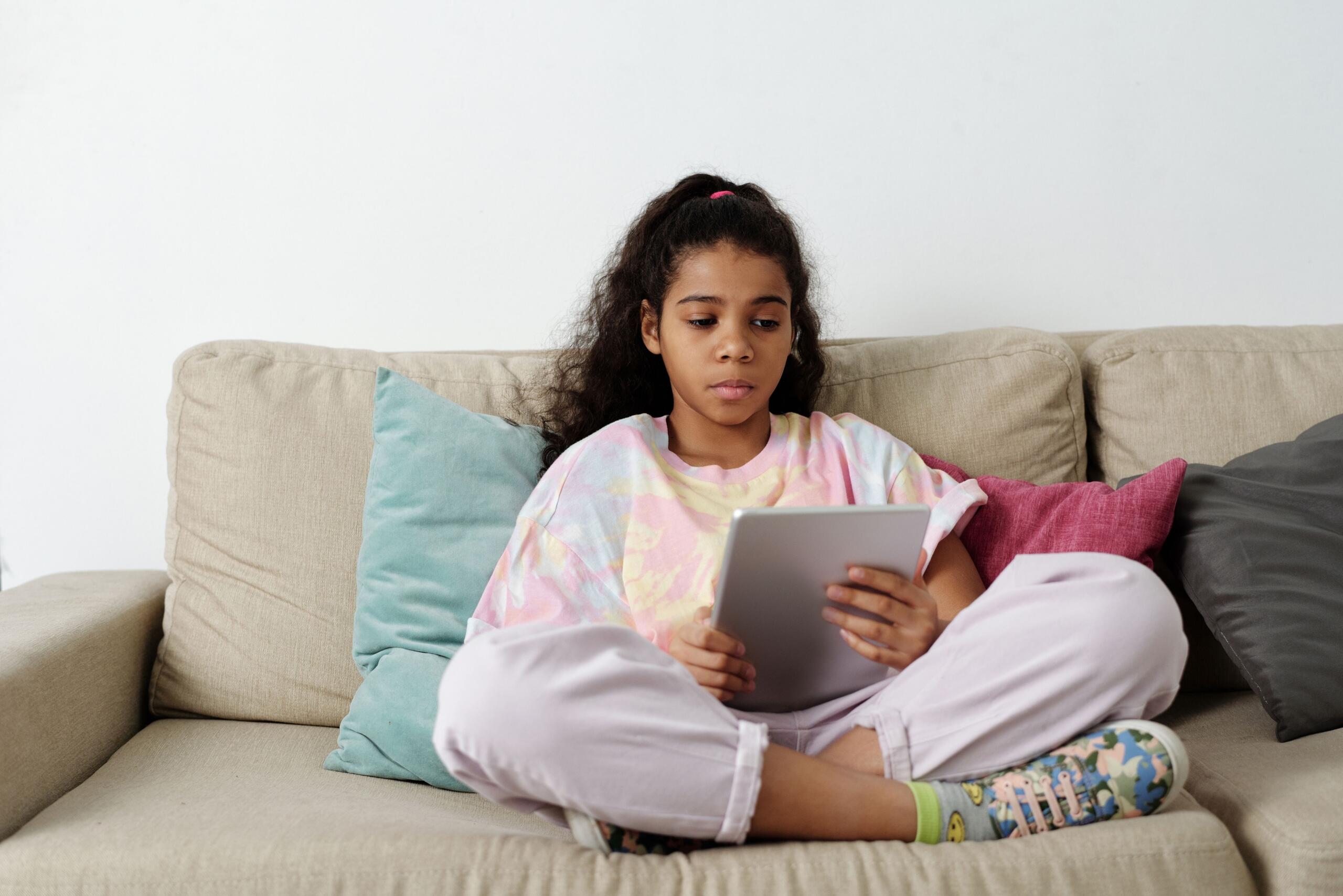 child sitting on a couch reading on e-reader
