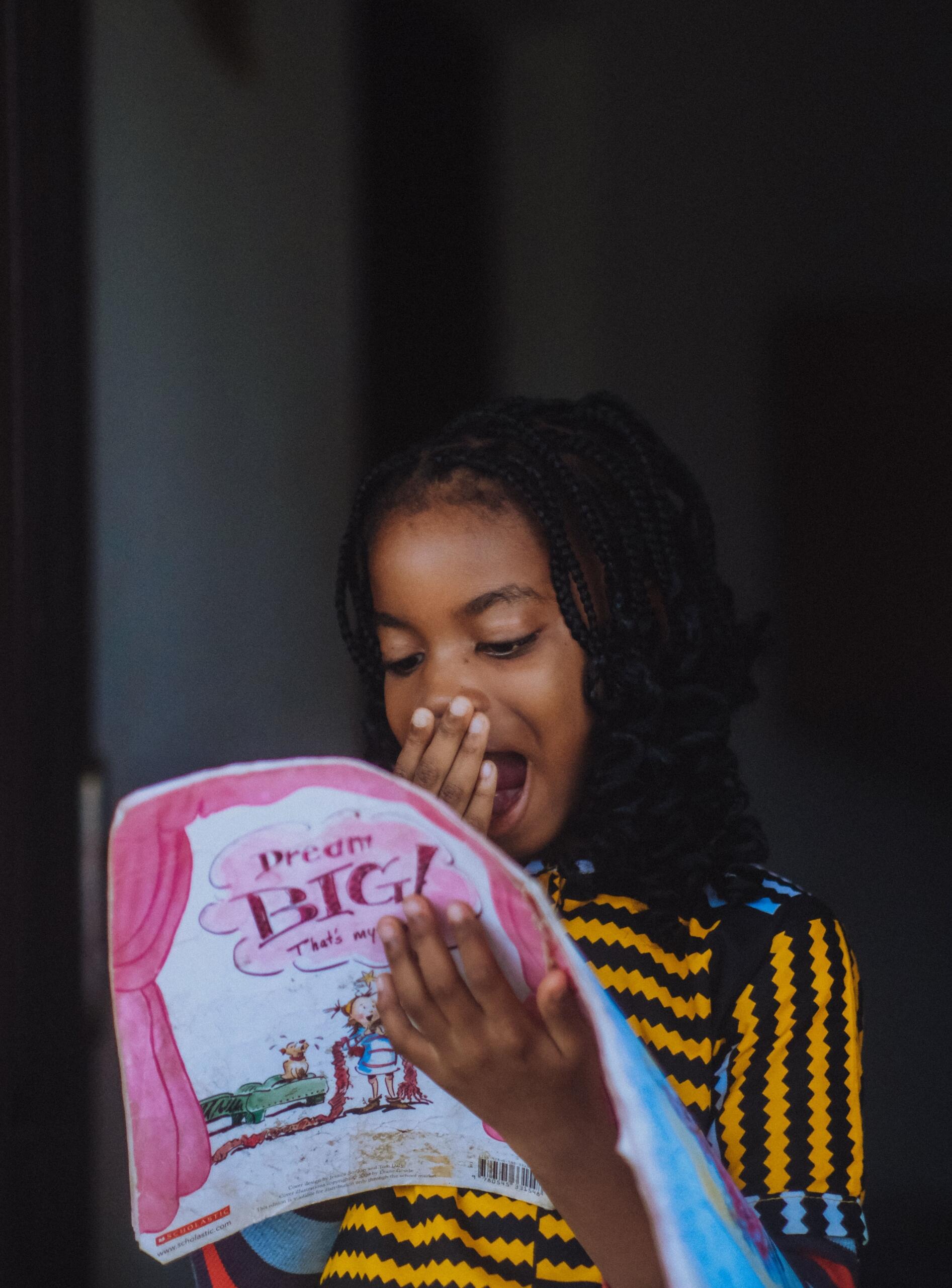 young girl holding a book with an expression of happy surprise on her face