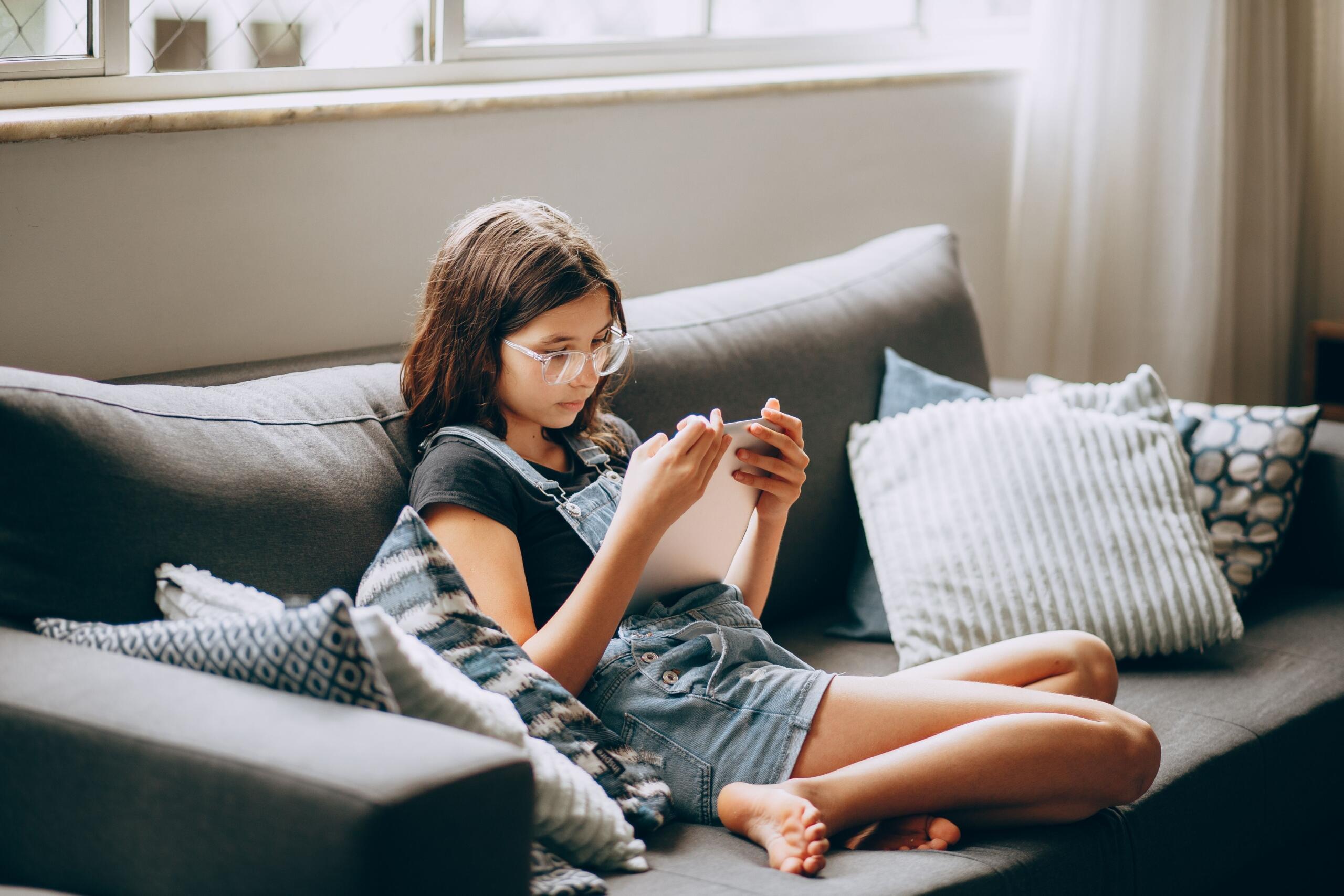 child sitting on a couch reading on digital device