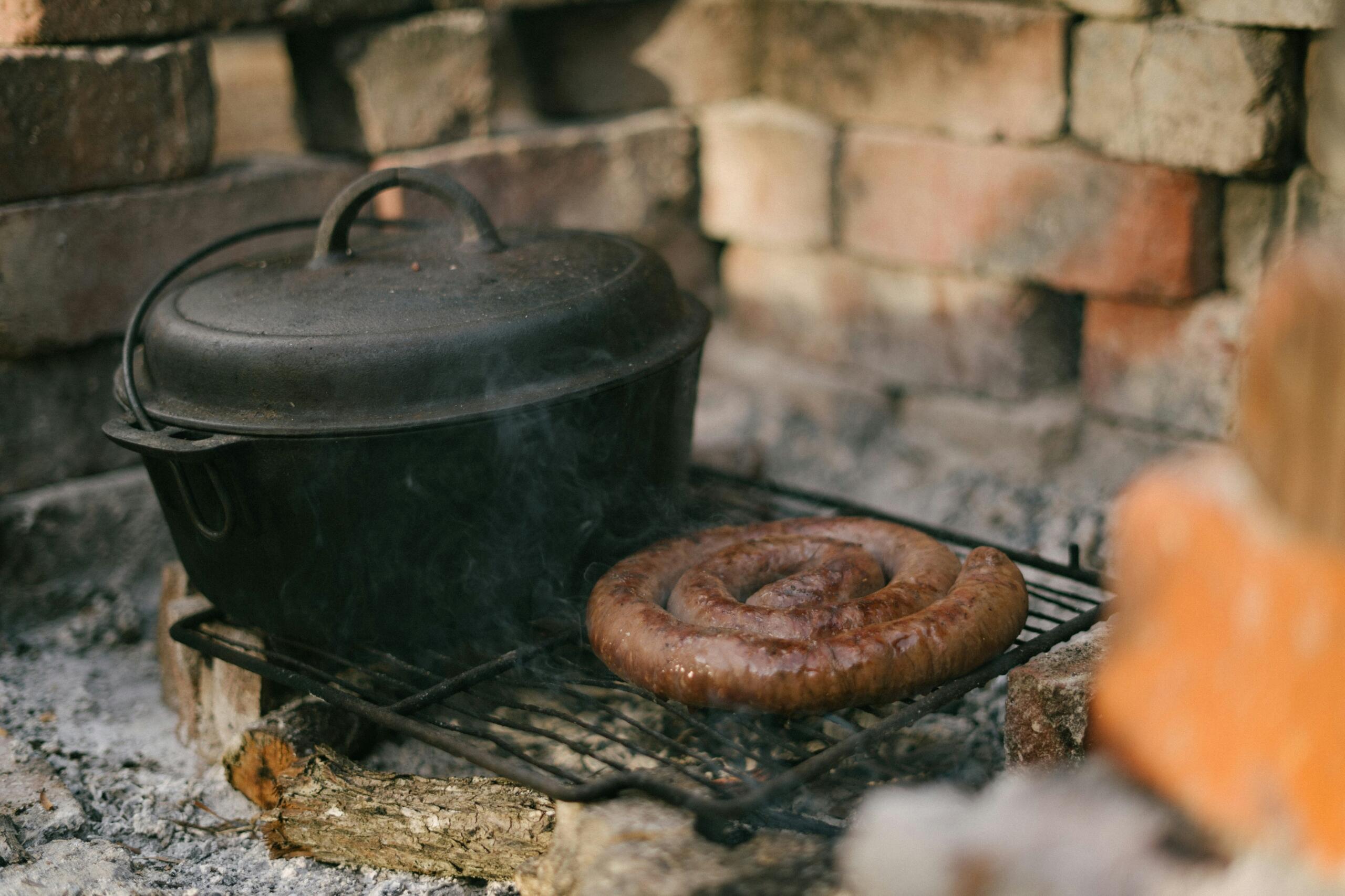 An image of a potjie pot with a side of boerewors on the braai.