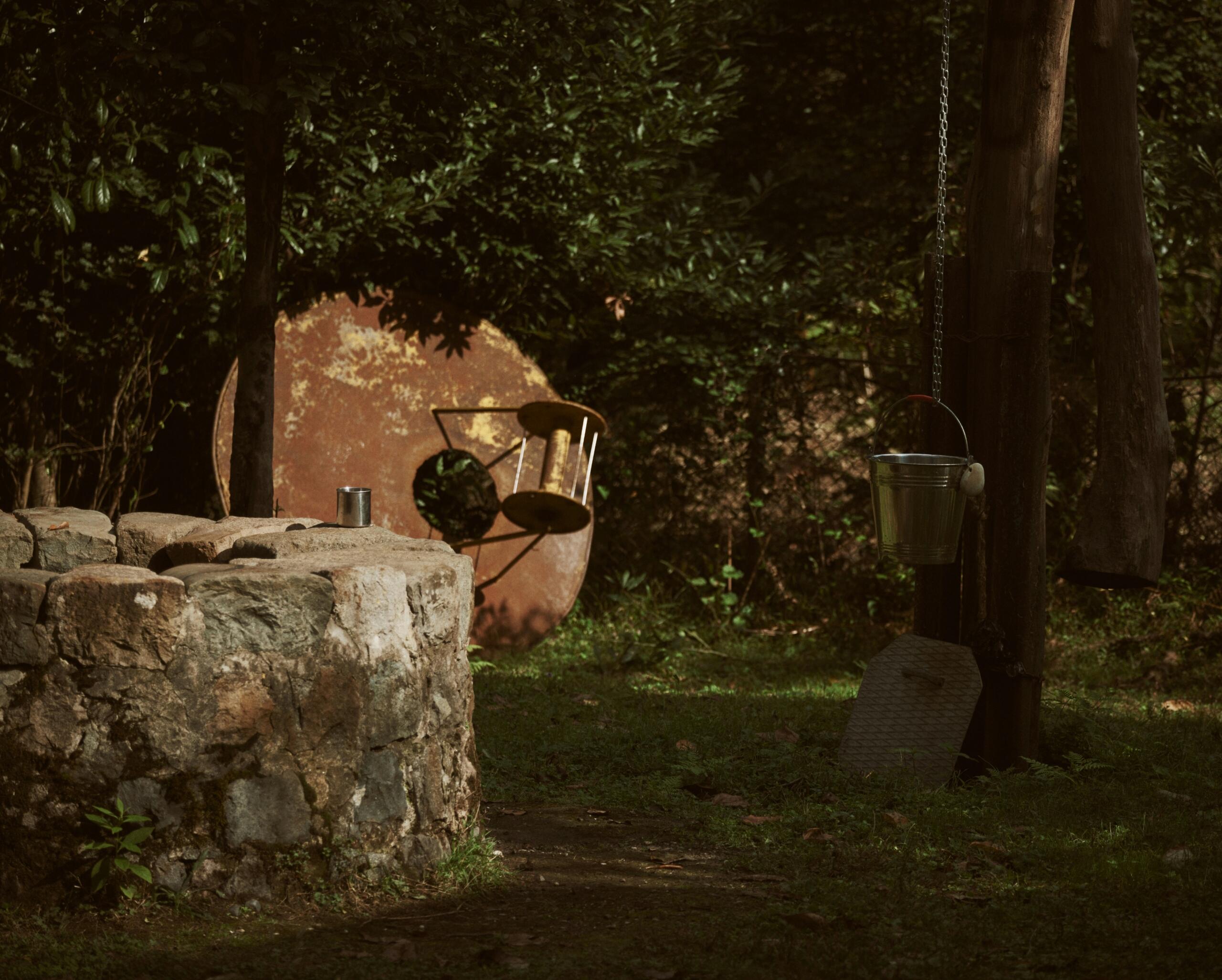 An old well with a bucket to the right of the well in the forest.
