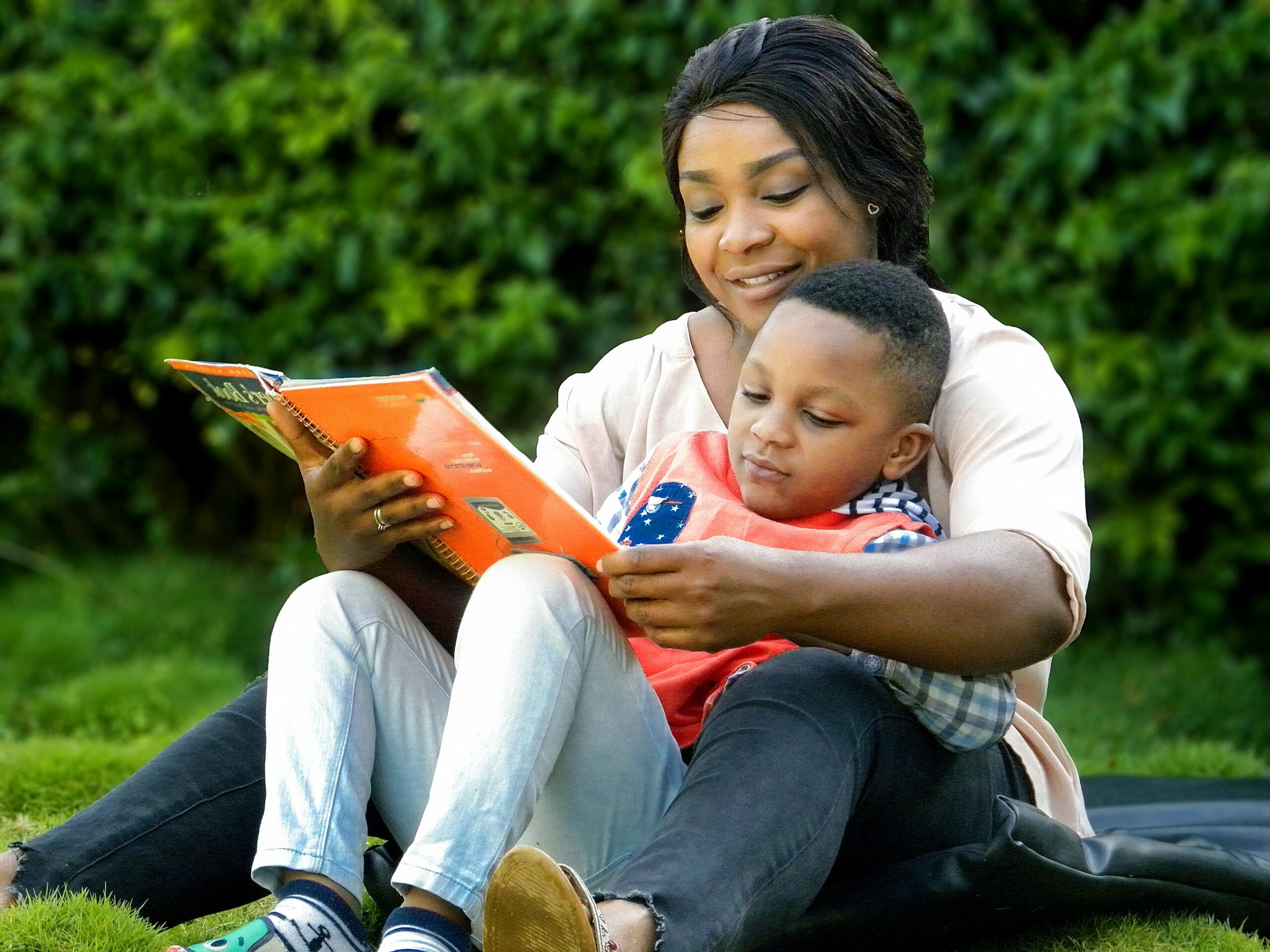 mother and child sitting on grass paging through a book together