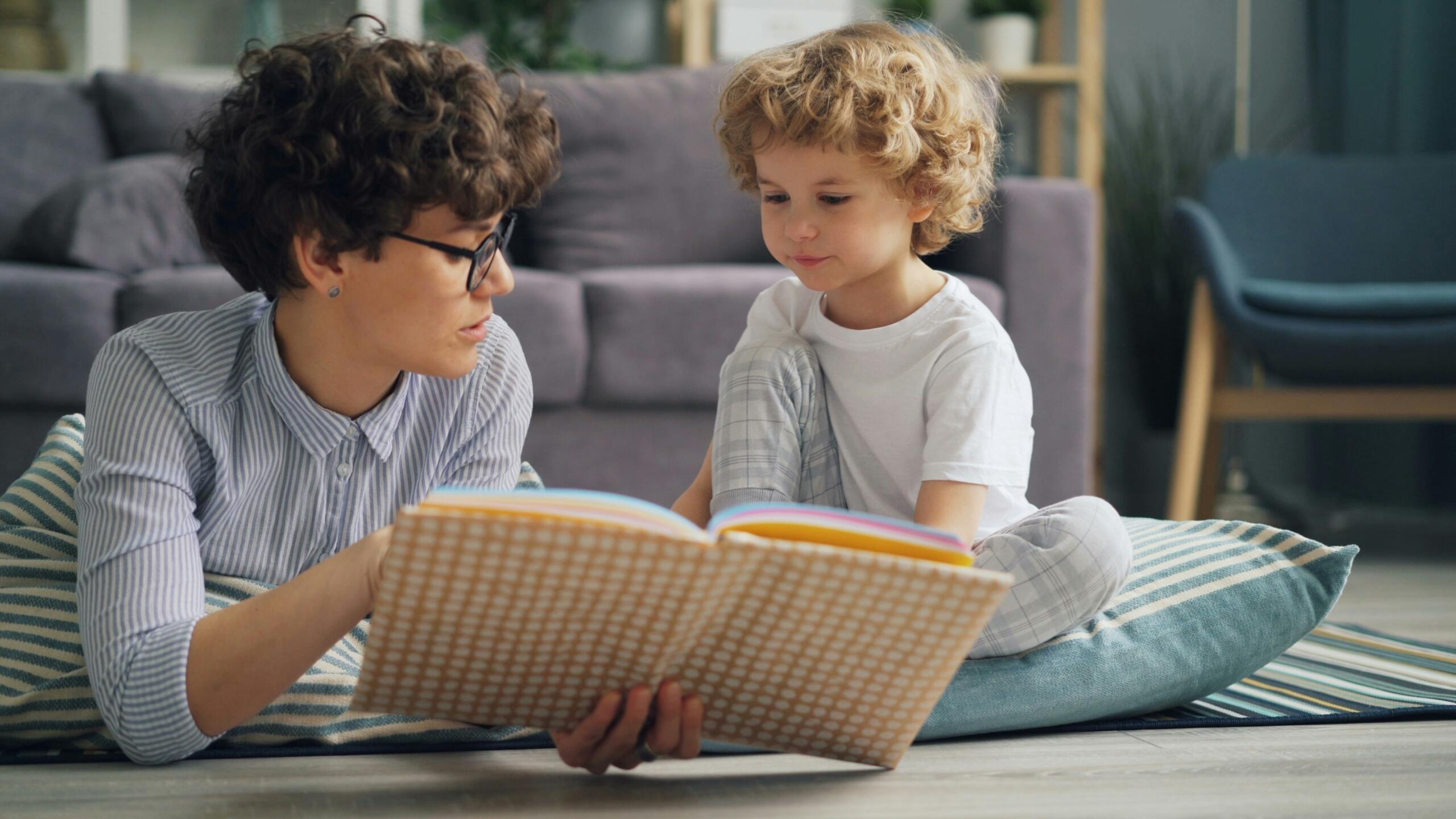 mother and child lying on the floor of the living room paging through a book together