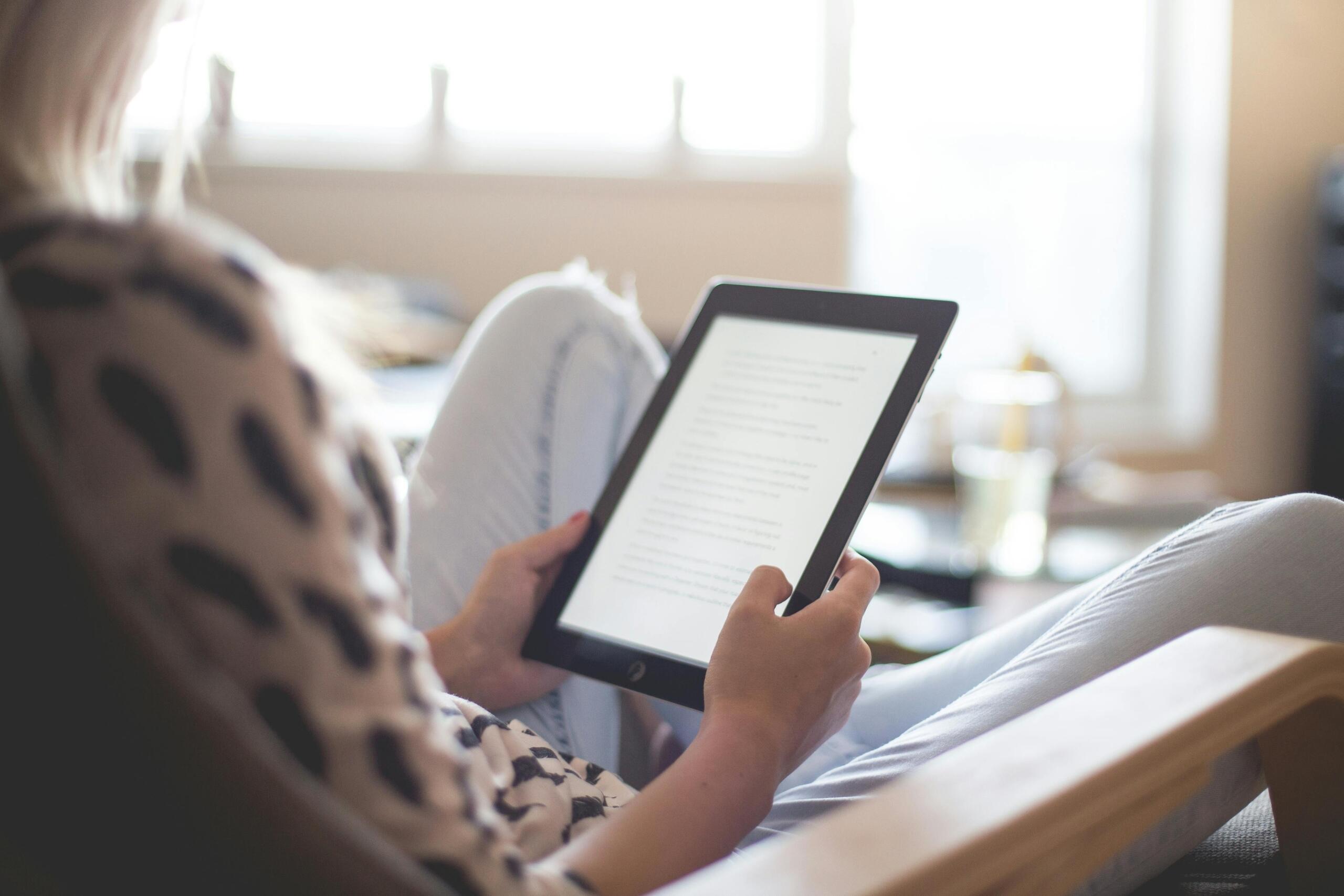 woman sitting on a couch reading on e-reader